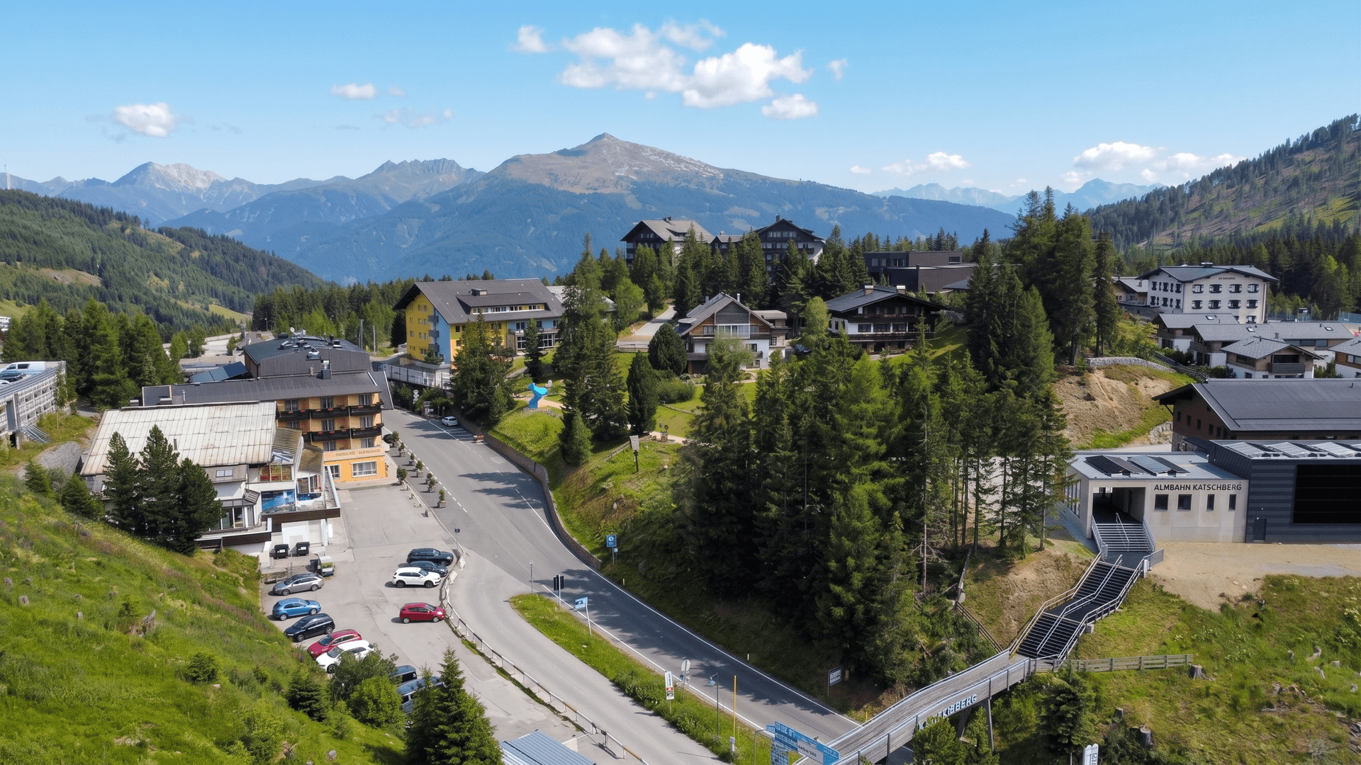 Weitläufige Luftaufnahme eines Bergdorfes mit Straßen, Gebäuden und Parkplätzen in den Alpen.