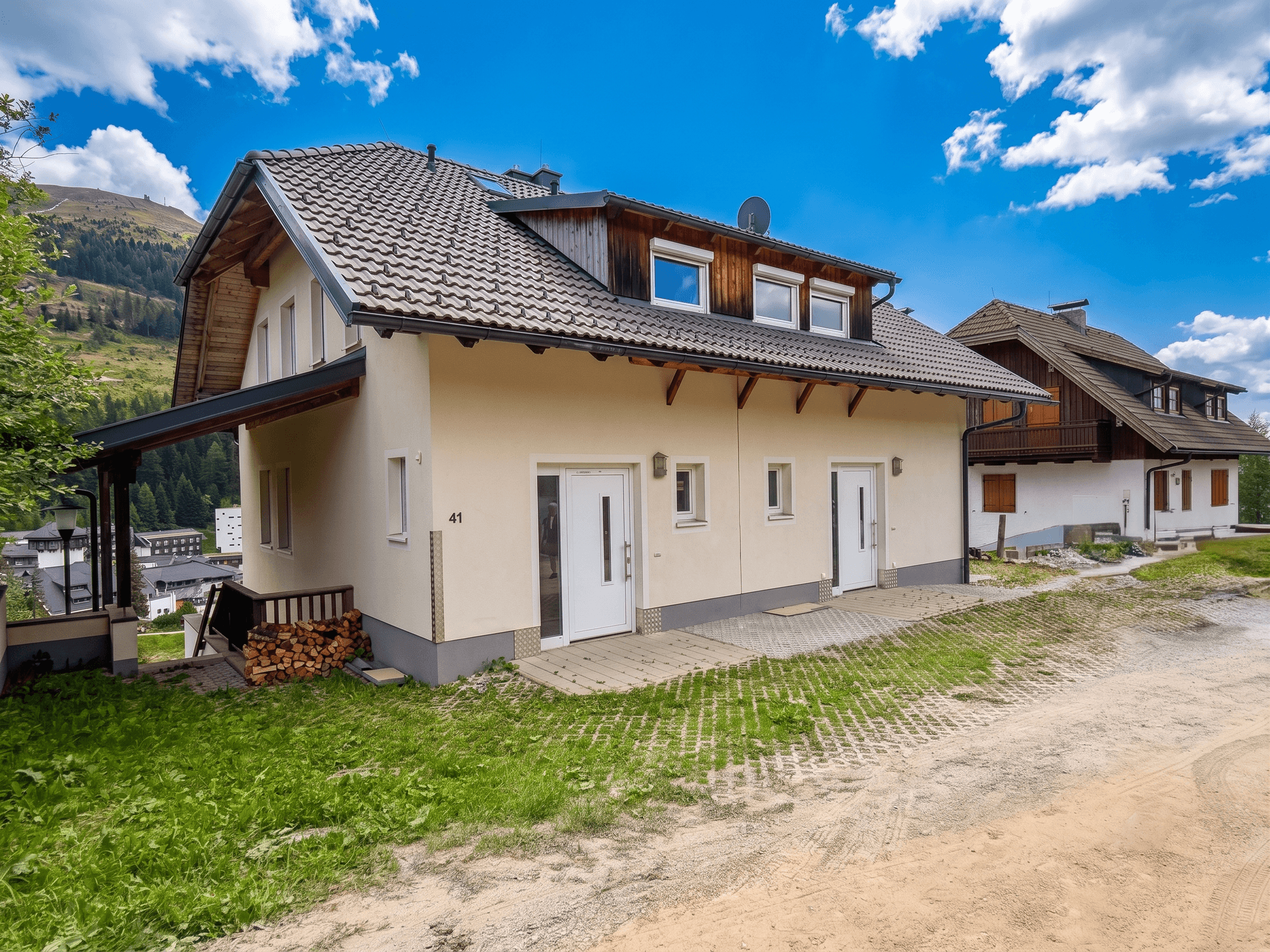 Vorderansicht des Hauses mit zwei Eingängen, gepflastertem Bereich und Holzstapel.