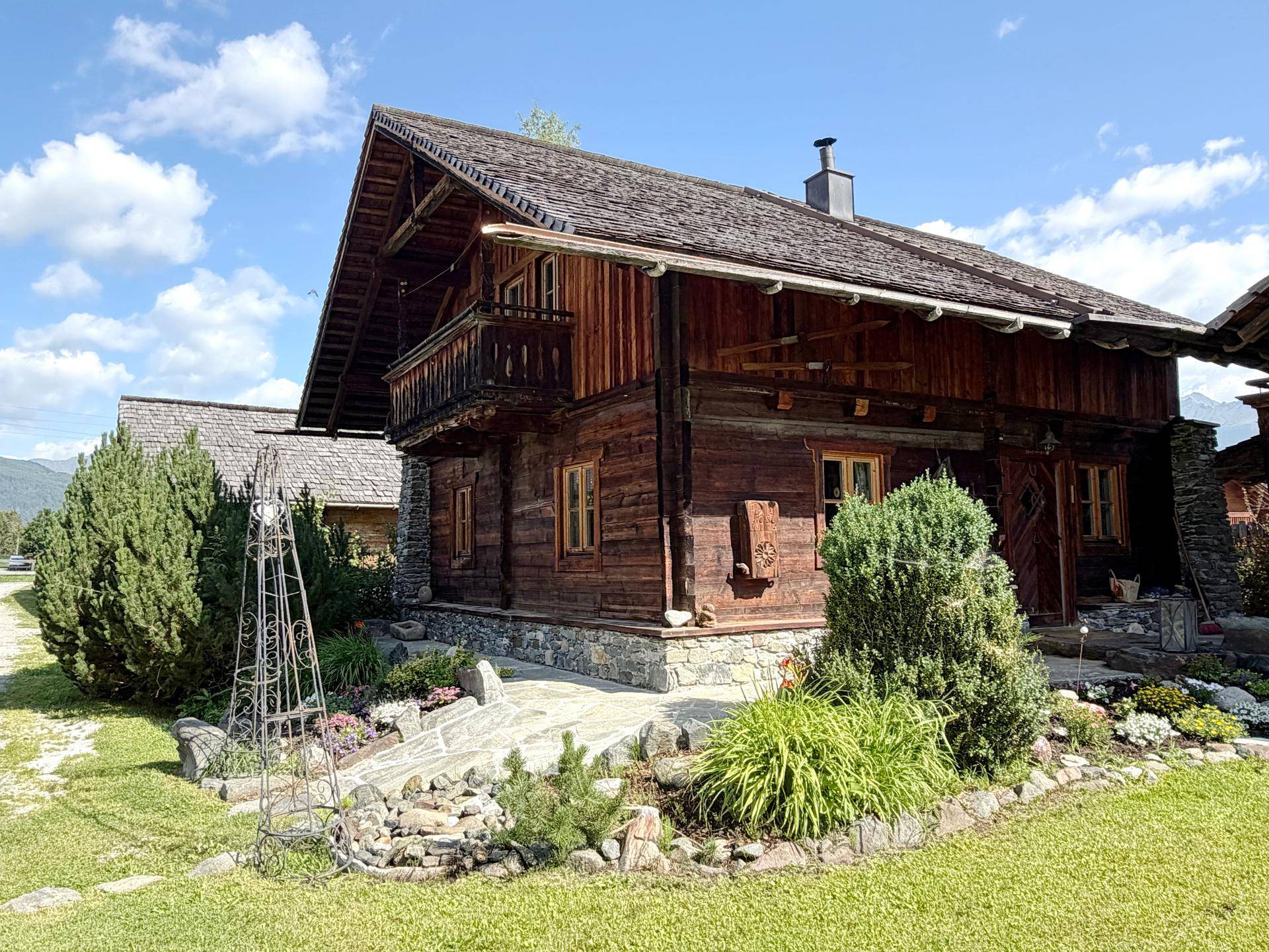 Charmantes Holzchalet mit traditioneller Architektur, umgeben von einem blühenden Garten und grünen Büschen.