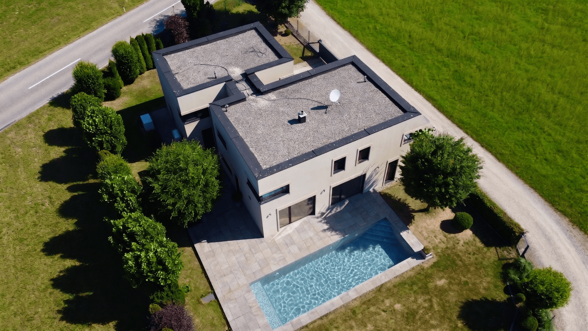 Luftaufnahme eines modernen Hauses mit Flachdach, Poolbereich und angrenzenden Grünflächen.