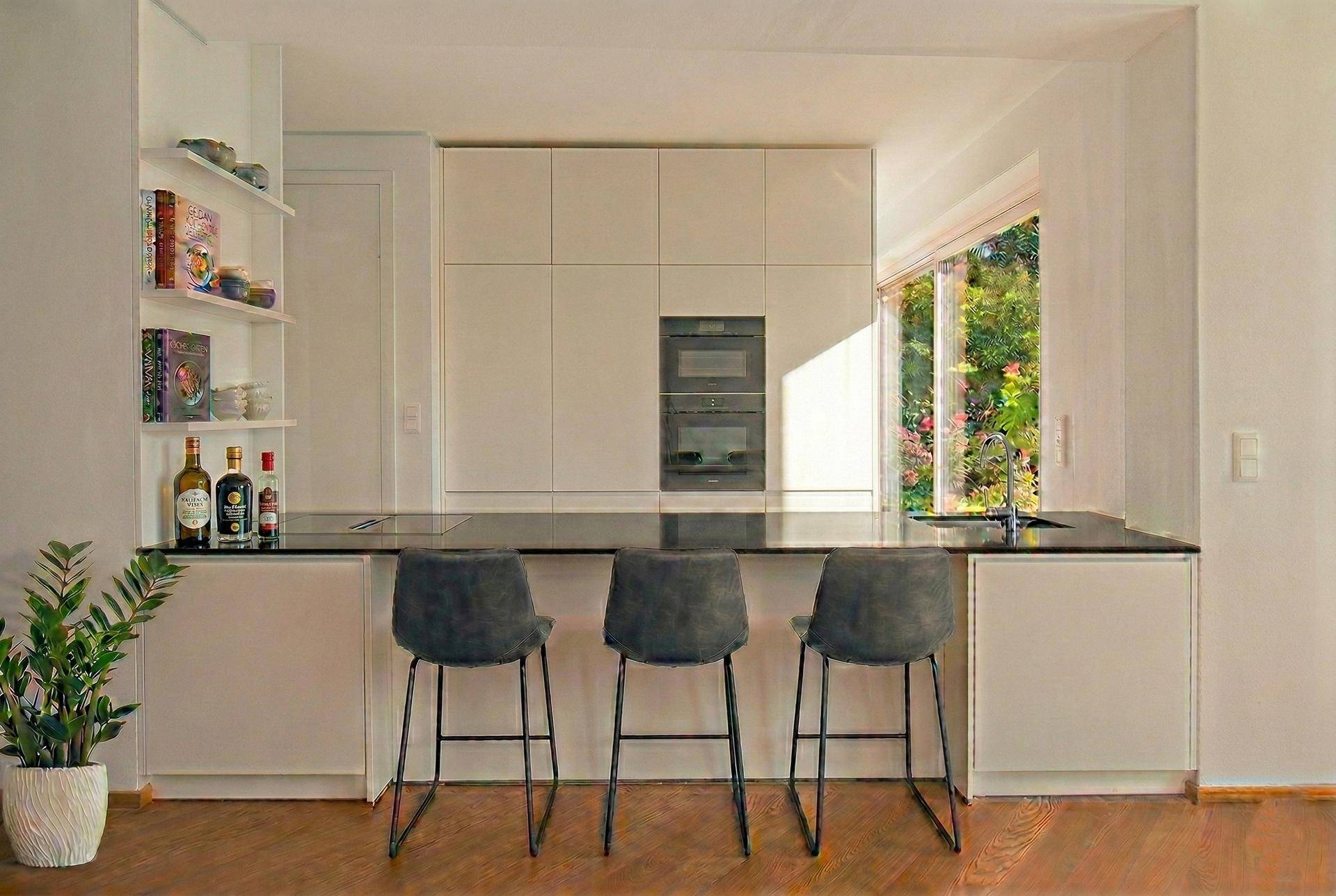 Moderne Küche mit weißen Schränken, dunkler Arbeitsplatte und integrierter Frühstücksbar mit Hockern.