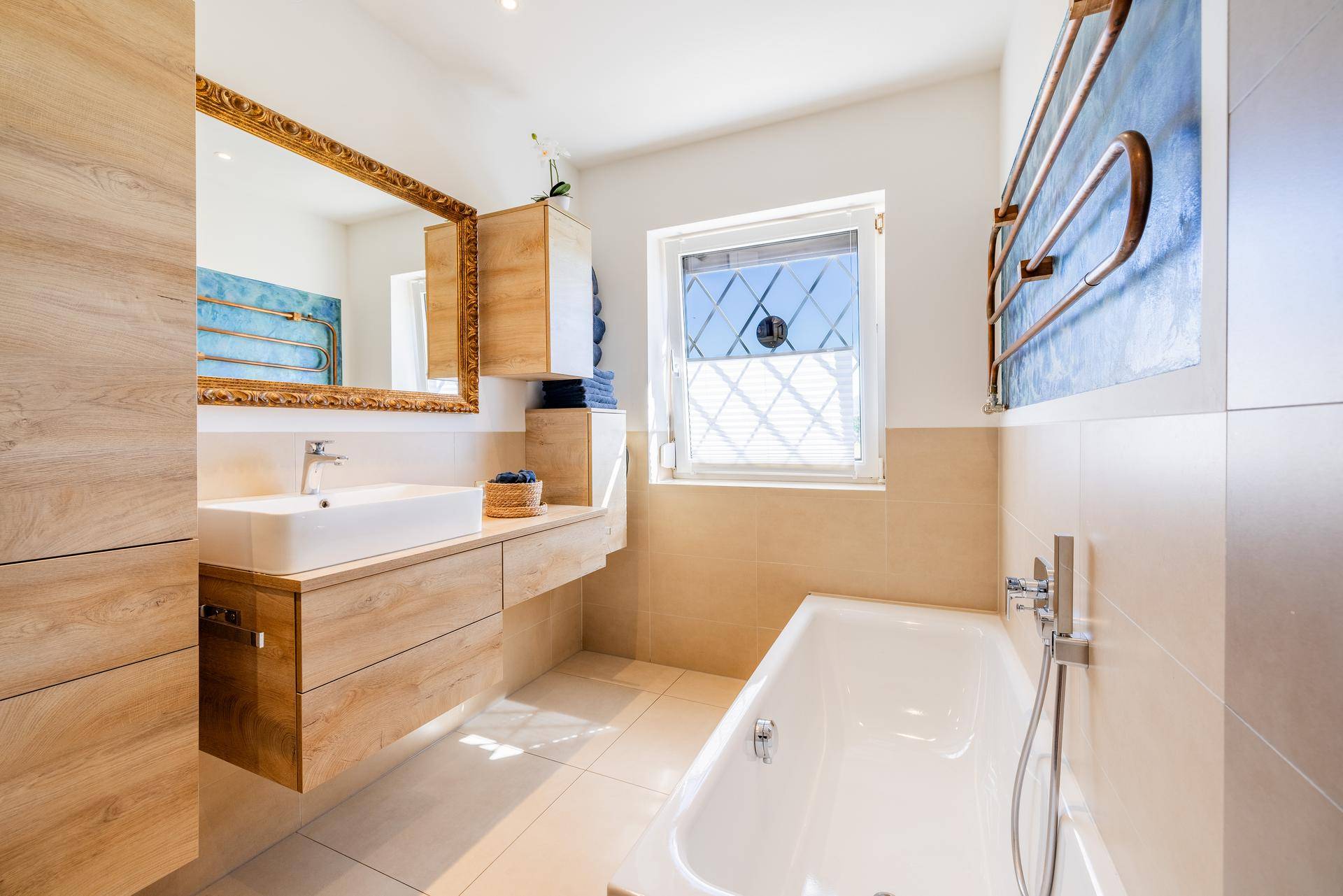 Modernes Badezimmer mit Badewanne, Einzelwaschbecken und beheiztem Handtuchhalter, hell durch ein Fenster.