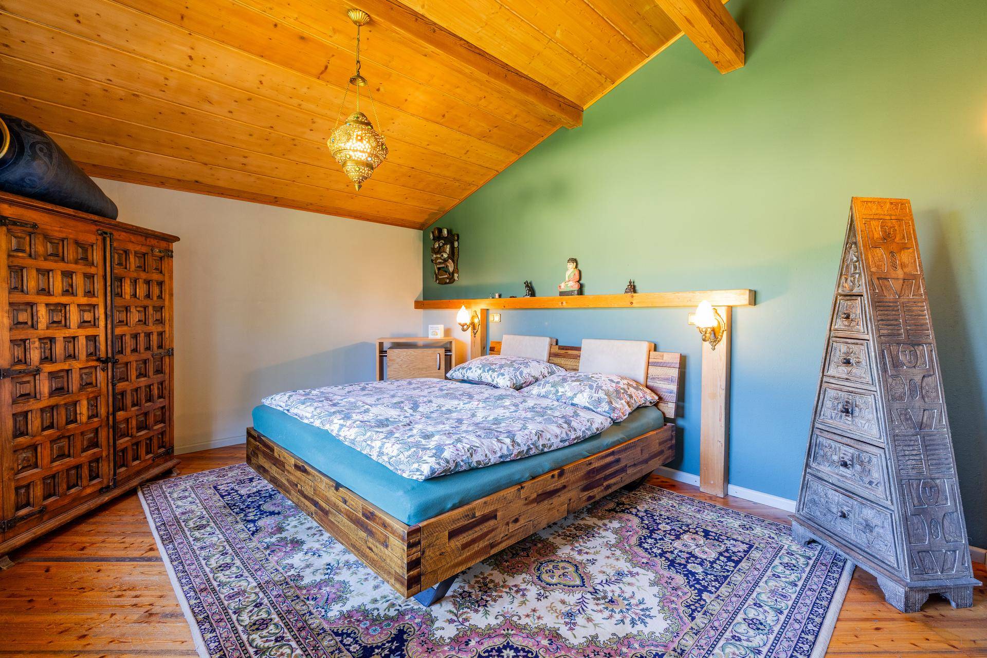 Gemütliches Schlafzimmer mit Holzbett, Holzbalkendecke und schrägen Wänden im Dachgeschoss.