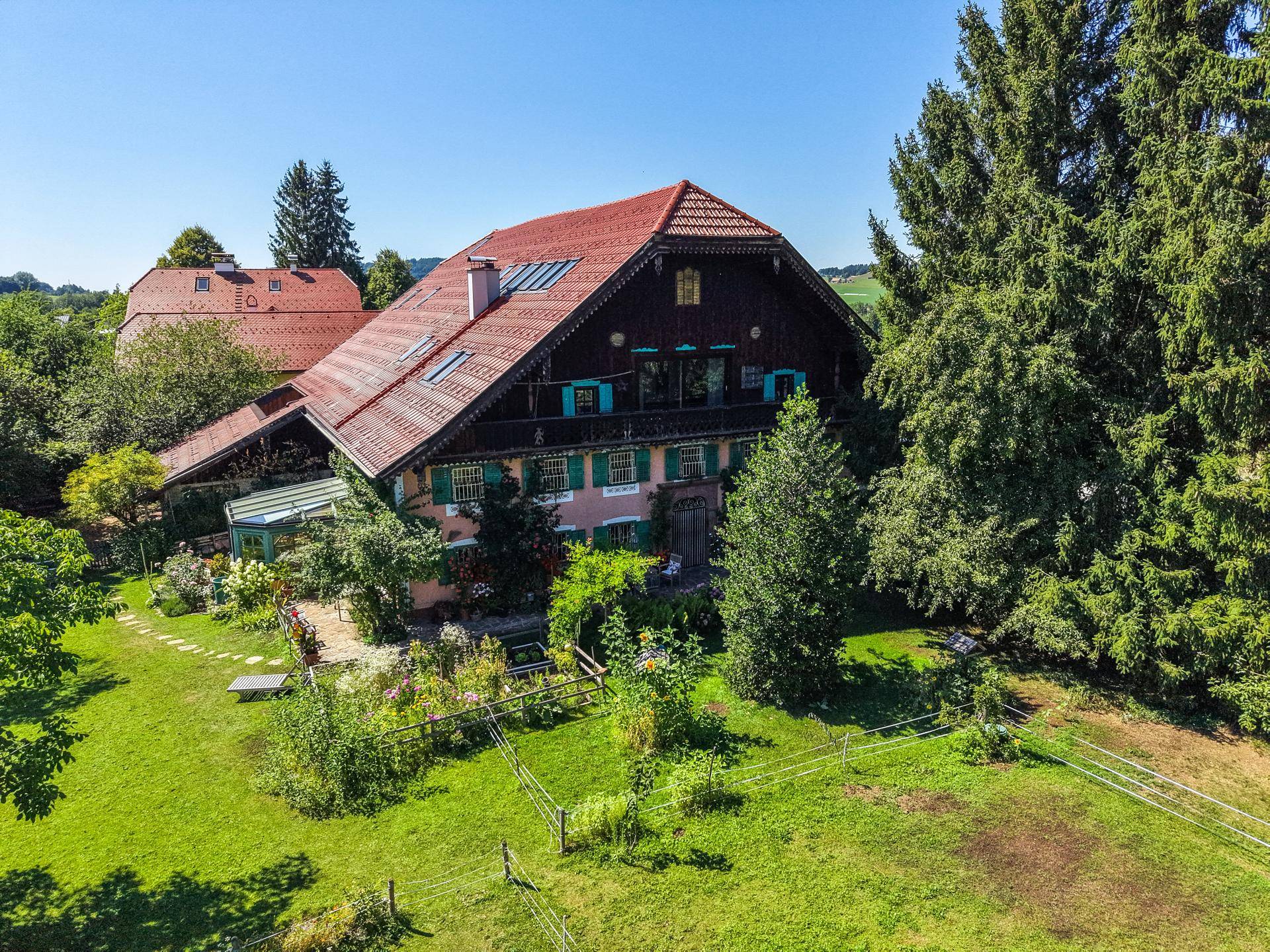 Malerisches traditionelles Haus mit rotem Ziegeldach, umgeben von üppigem Grün und Bäumen.