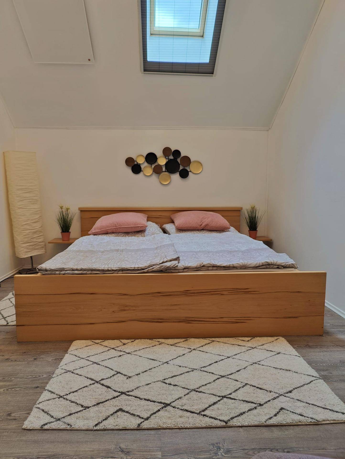 Gemütliches Schlafzimmer mit Holzbett, Dachfenster und schräger Decke für viel Tageslicht.
