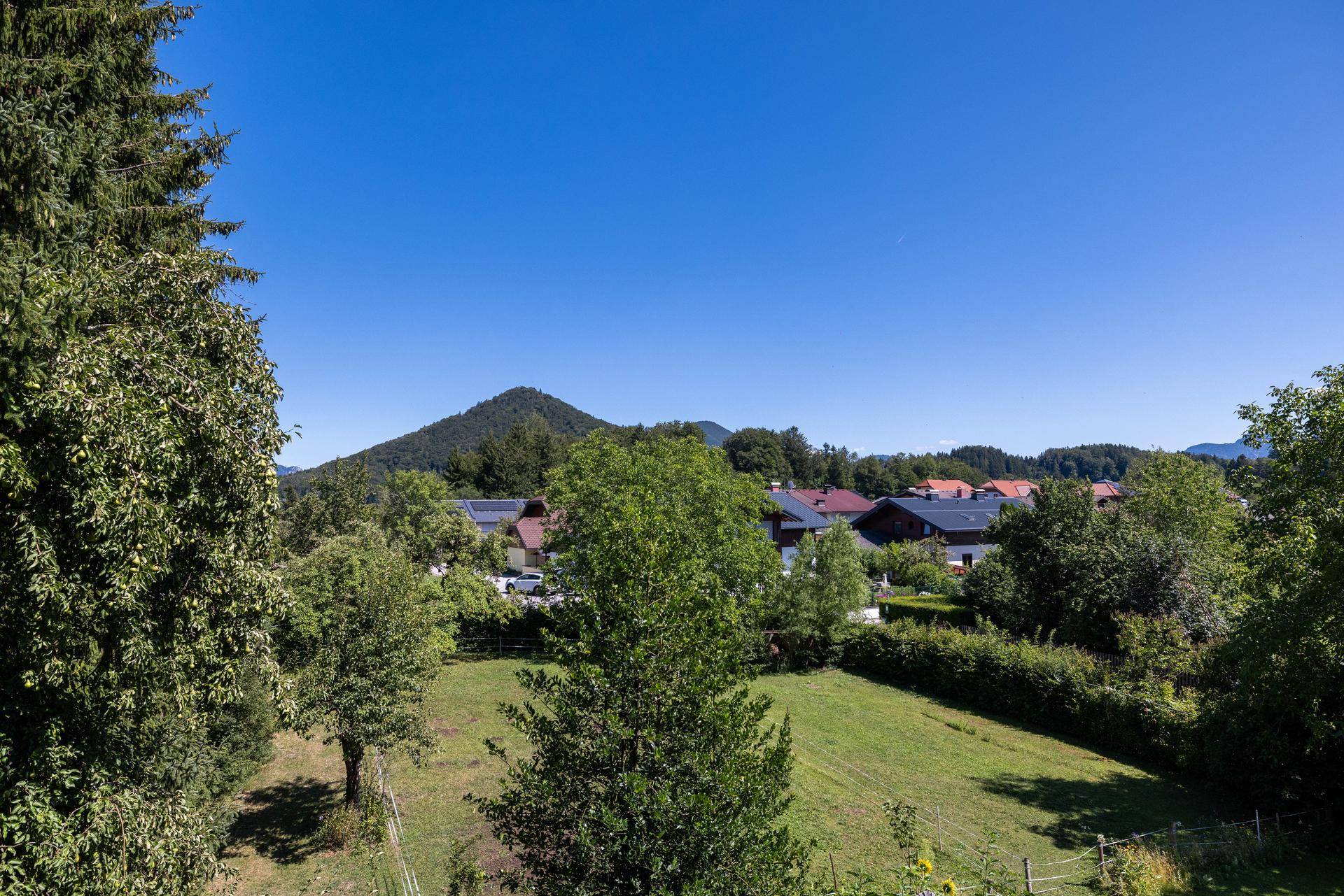 Weitläufiger Blick über grüne Felder, Bäume und eine ländliche Siedlung unter blauem Himmel.
