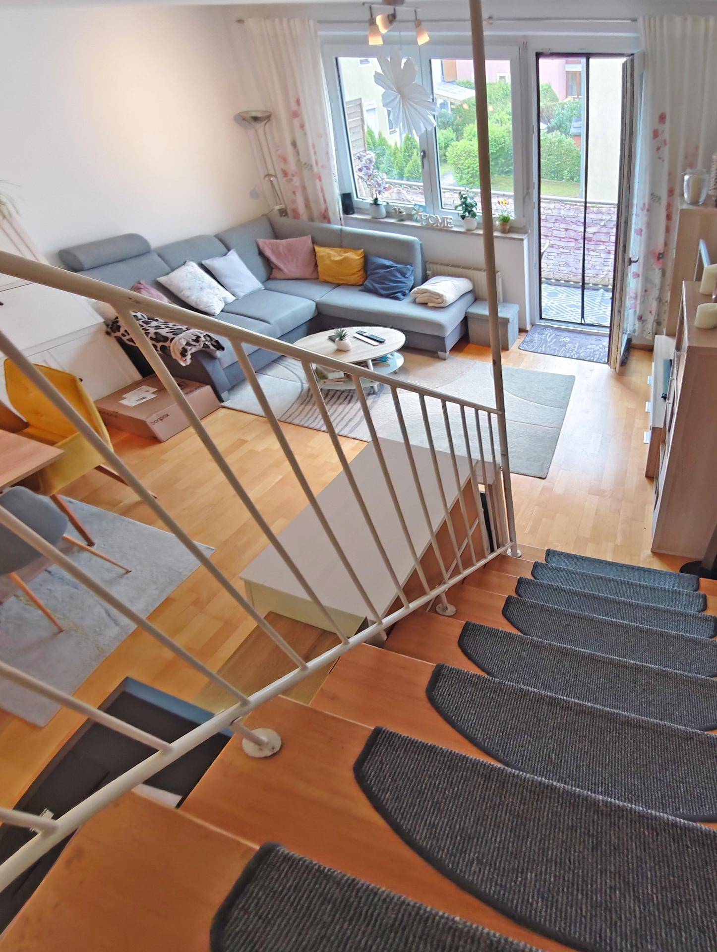 Blick von der Treppe in das helle Wohnzimmer mit Sofa und Zugang zum Außenbereich.