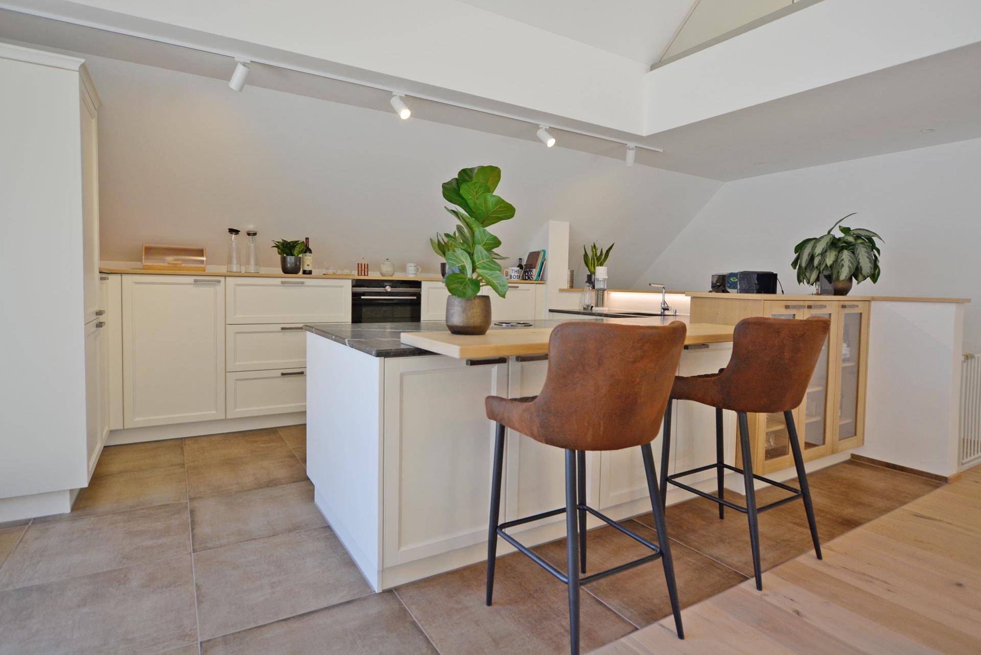 Moderne Küche mit weißer Einbauküche, Kücheninsel und Fliesenboden, offen zum Wohnbereich.