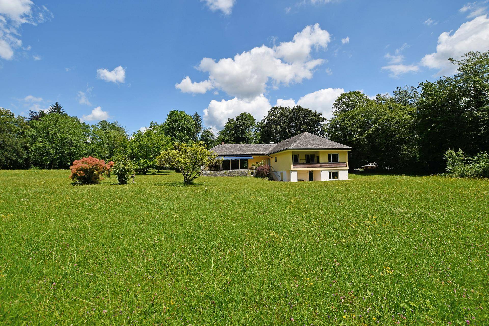 Geräumiges Grundstück mit einem gelben Haus und üppiger Vegetation unter strahlendem Sonnenschein.