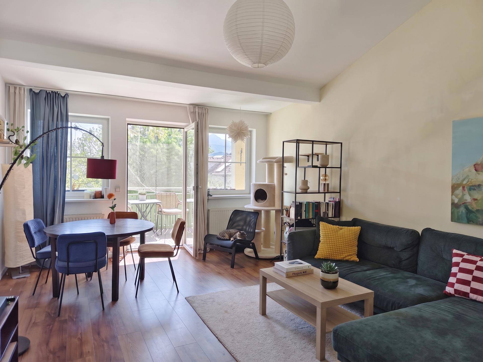 Gemütlicher Wohn-Essbereich mit Holzboden, Sofa, Esstisch und Zugang zu einem sonnigen Balkon.