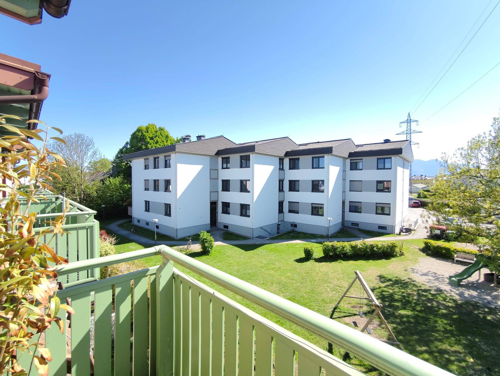 Blick vom Balkon auf ein weiteres Wohngebäude, eine grüne Rasenfläche und einen Spielplatz.