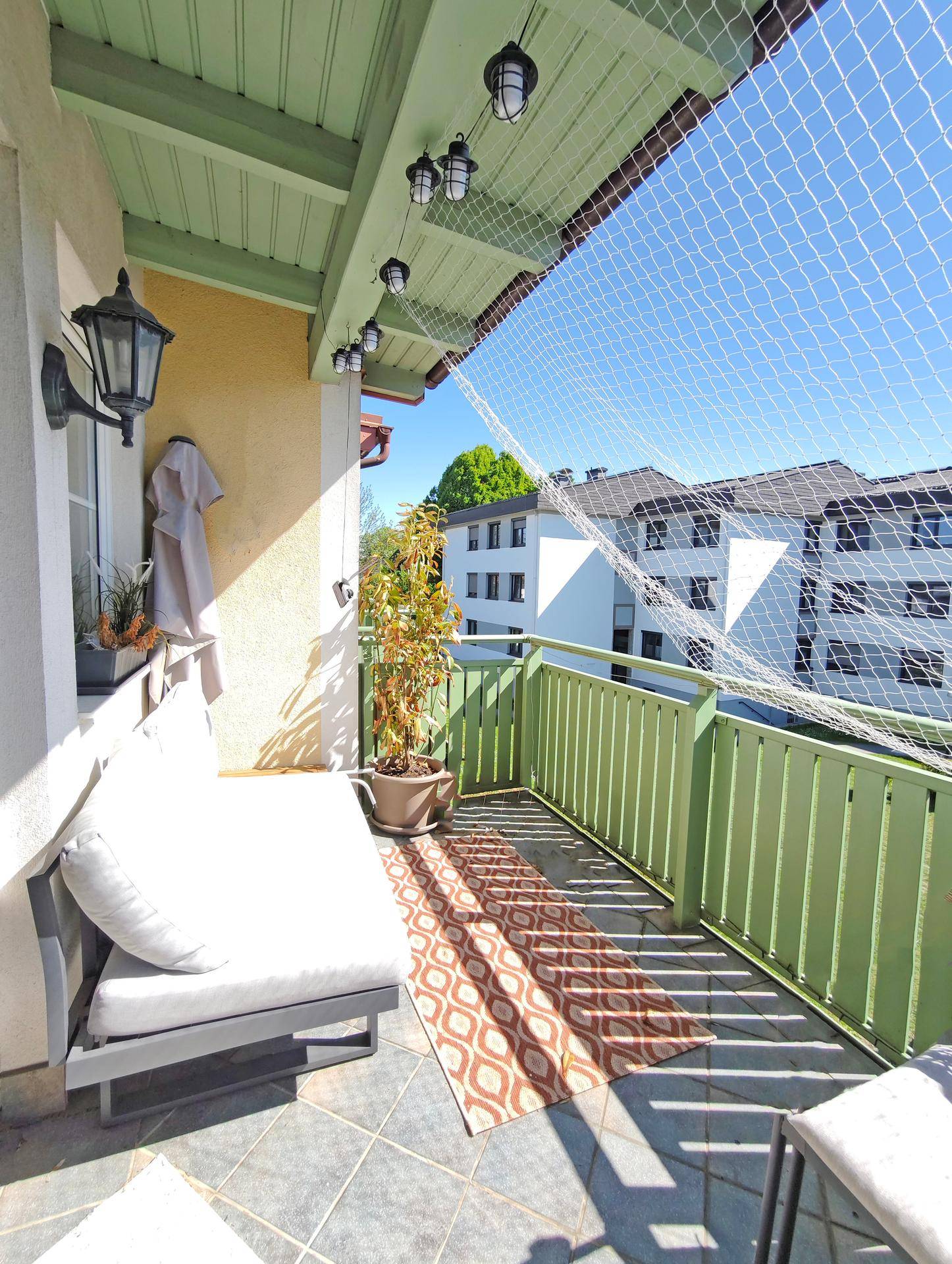 Möblierter Balkon mit Fliesenboden, Sitzgelegenheiten und einem Sicherheitsnetz, ideal zum Entspannen.