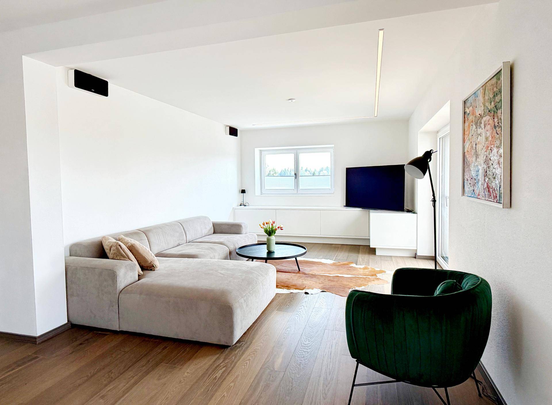 Helles Wohnzimmer mit beigem Ecksofa, Holzboden und Blick ins Grüne.