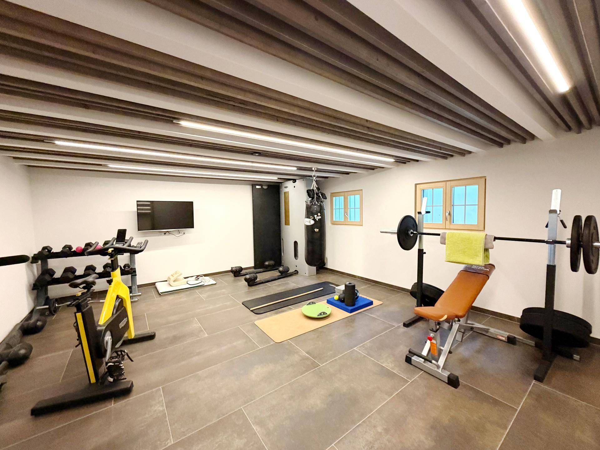 Gut ausgestatteter Fitnessraum mit verschiedenen Trainingsgeräten und Holzbalkendecke.