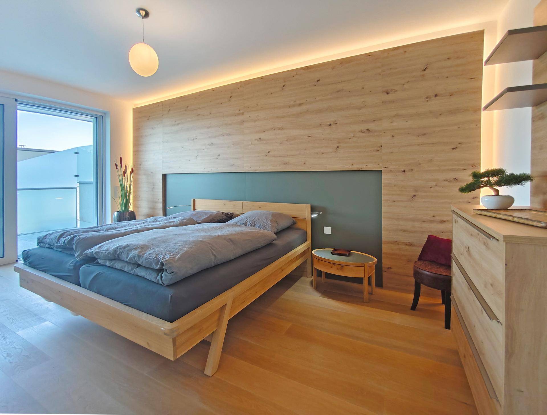 Helles Schlafzimmer mit Holzbett, Holzwandverkleidung und direktem Zugang zu einem Balkon oder einer Terrasse.