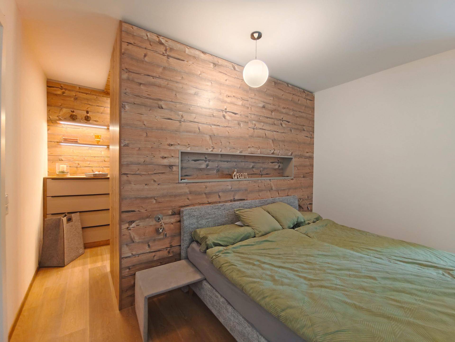 Gemütliches Schlafzimmer mit Holzwandverkleidung, Doppelbett und offenem Zugang zu einem begehbaren Kleiderschrank.