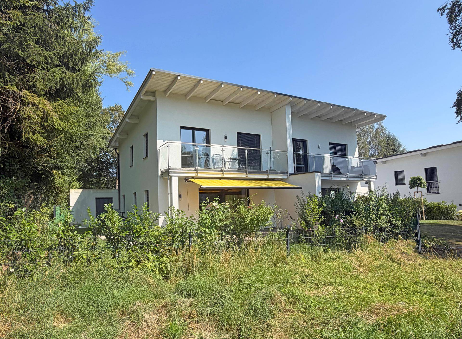 Ansicht des modernen Hauses mit Balkonen und umliegender grüner Landschaft an einem sonnigen Tag.