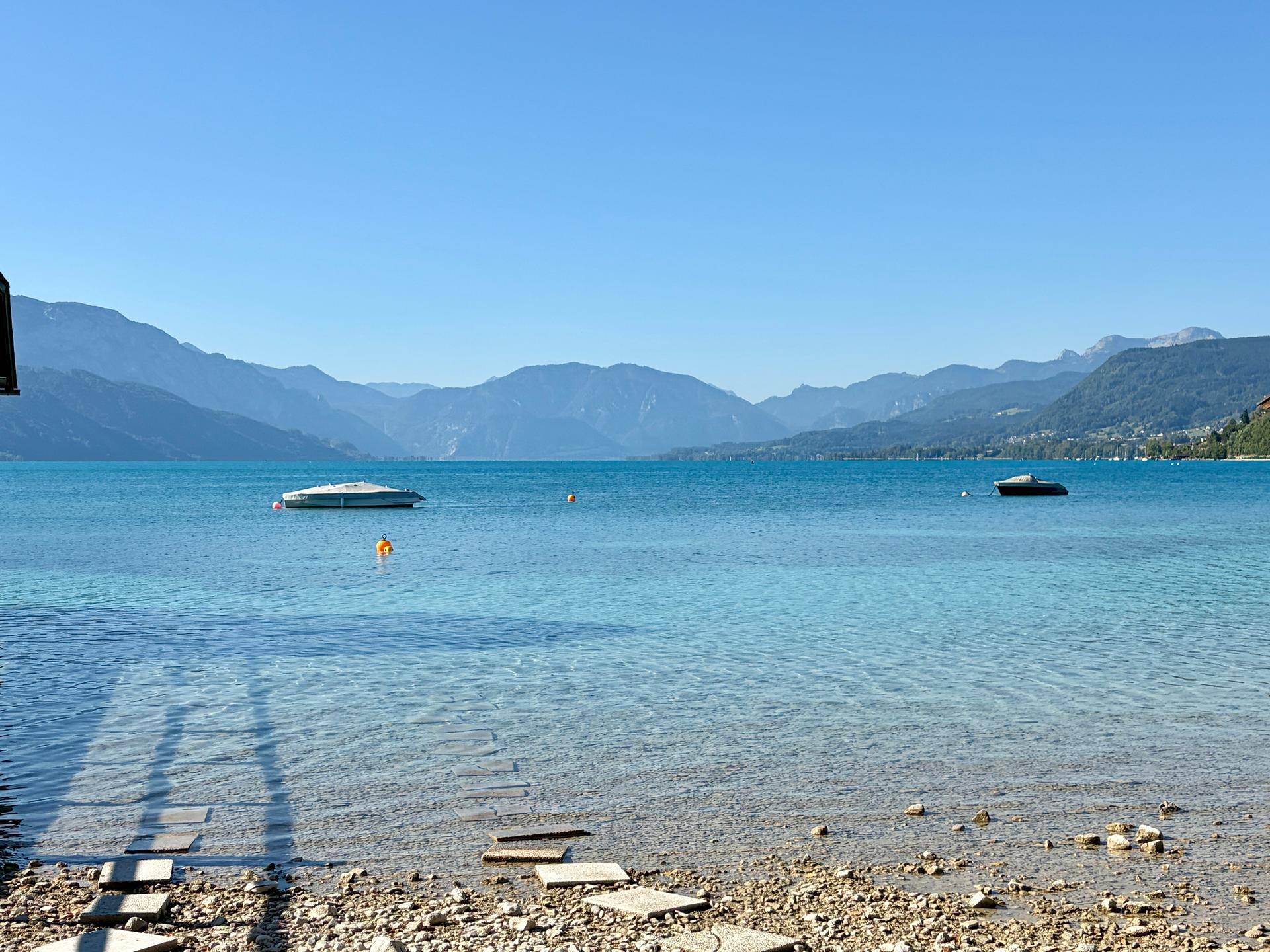Klarer See mit majestätischen Bergen im Hintergrund unter einem strahlend blauen Himmel.