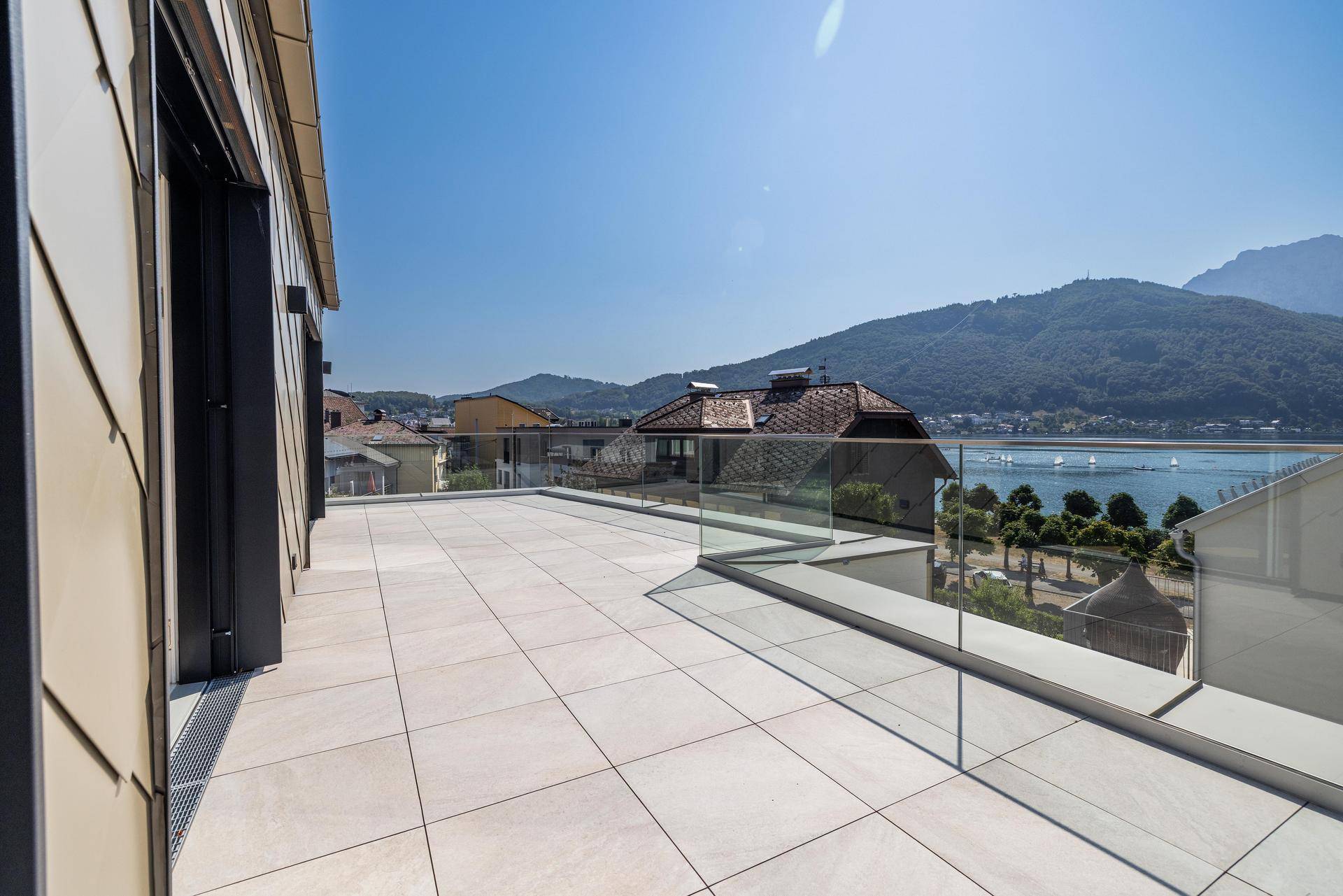 Geräumige Terrasse mit modernen Fliesen und atemberaubendem Blick auf den See und die bewaldeten Hügel.