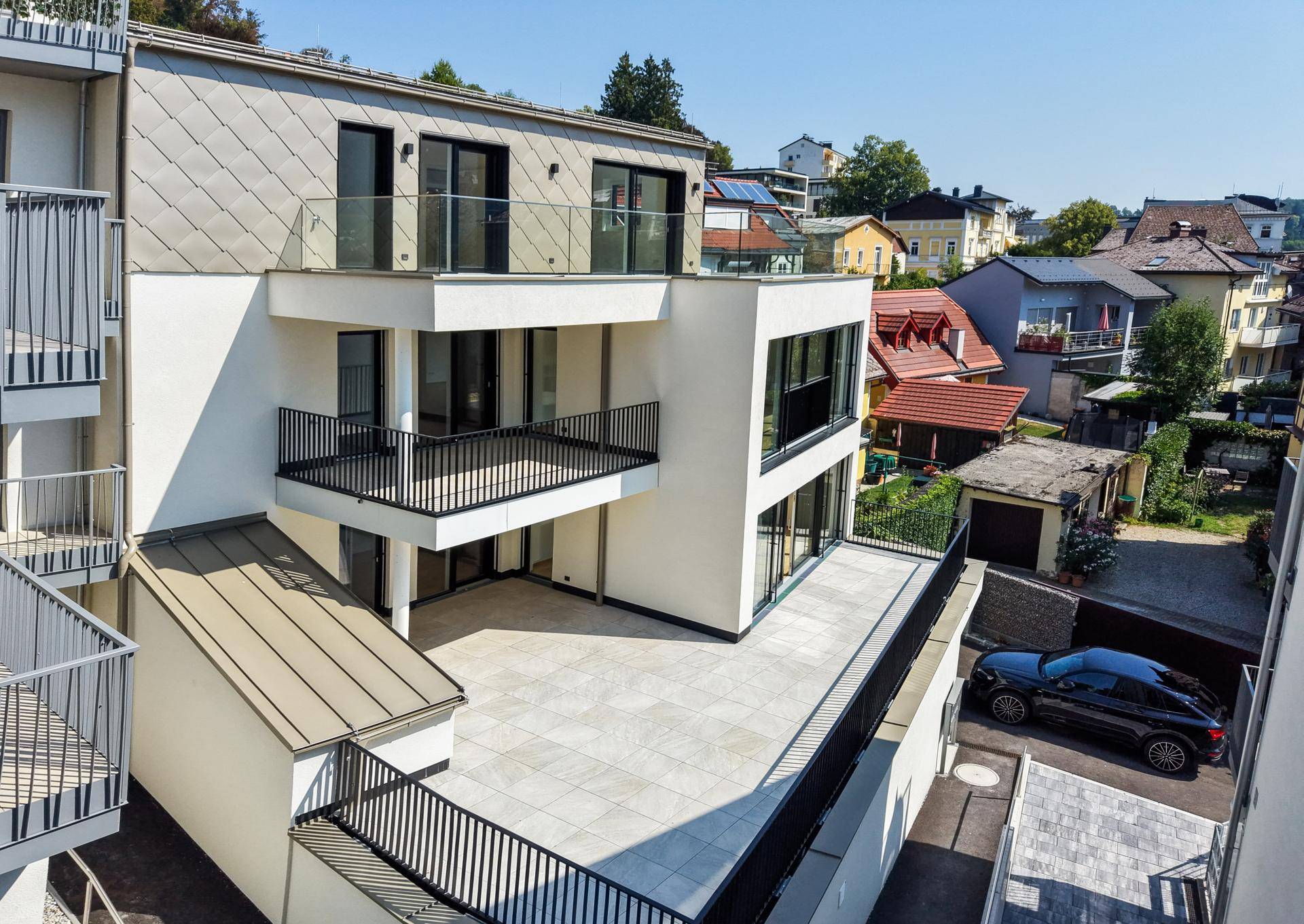 Moderne Architektur mit mehreren Terrassen und Balkonen, eingebettet in eine Wohngegend mit viel Grün.