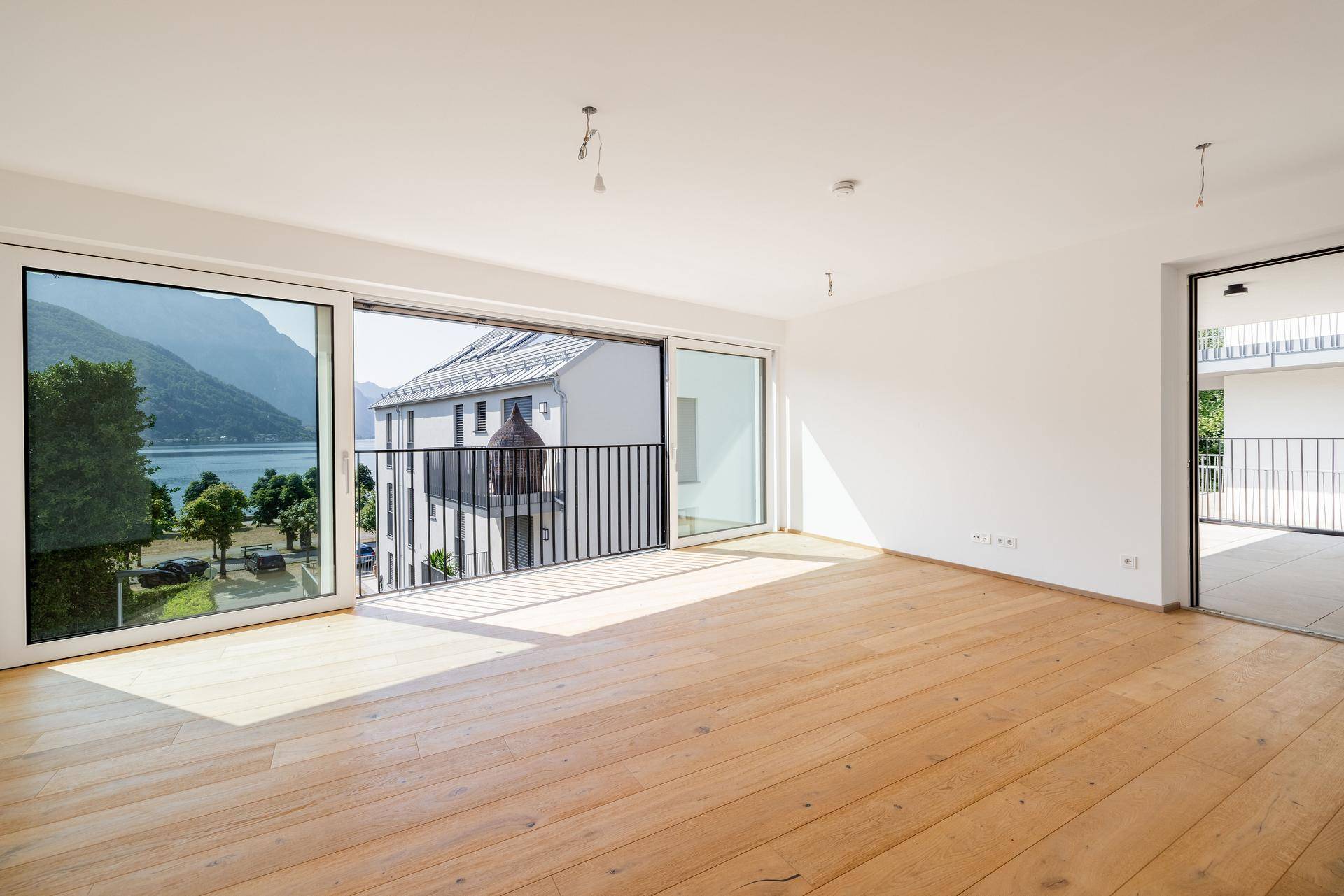 Lichtdurchfluteter Wohnbereich mit Holzboden und direktem Zugang zum Balkon mit Seeblick.