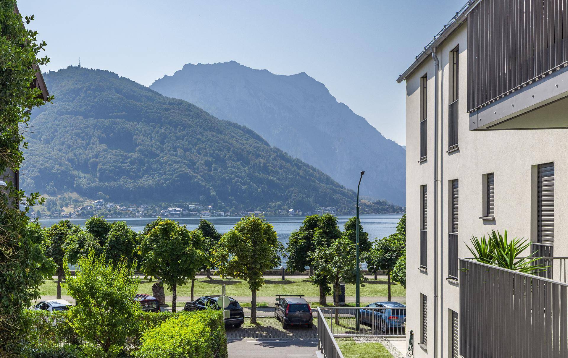 Panoramablick auf den See und die umliegenden Berge von einem Balkon oder Fenster aus.