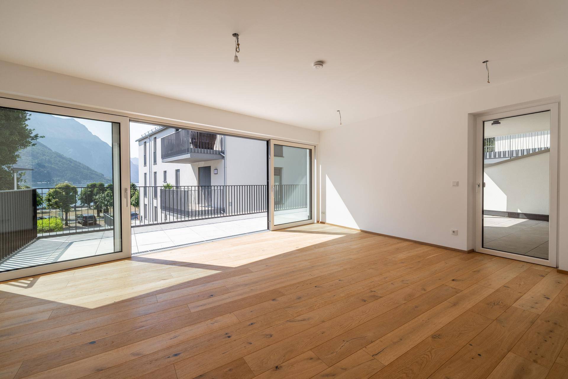 Heller Wohnraum mit Eichenparkett und großen Schiebetüren, die zu einem Balkon mit Seeblick führen.