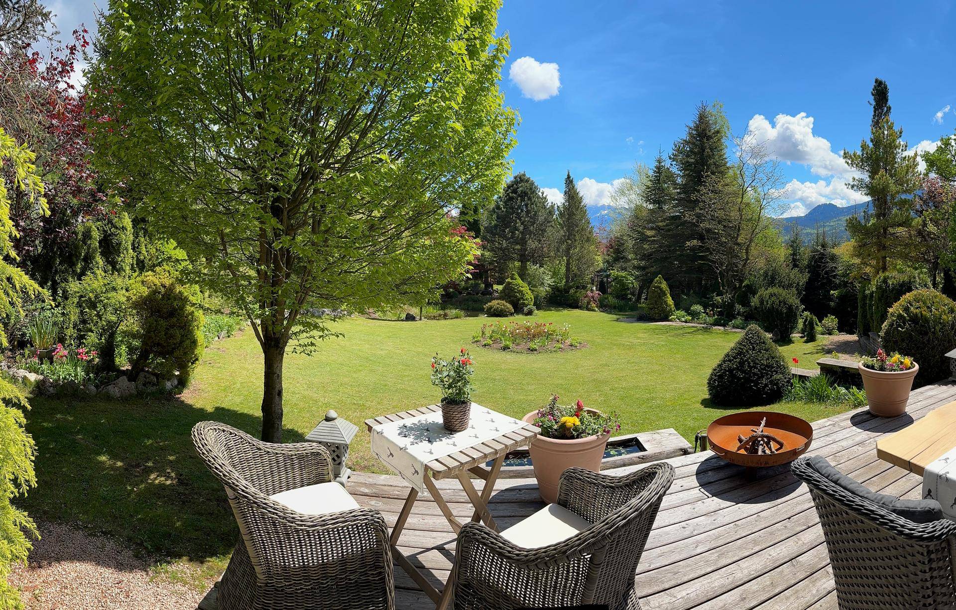 Gemütliche Holzterrasse mit Sitzgelegenheiten und weitem Blick über den gepflegten Garten und die Landschaft.