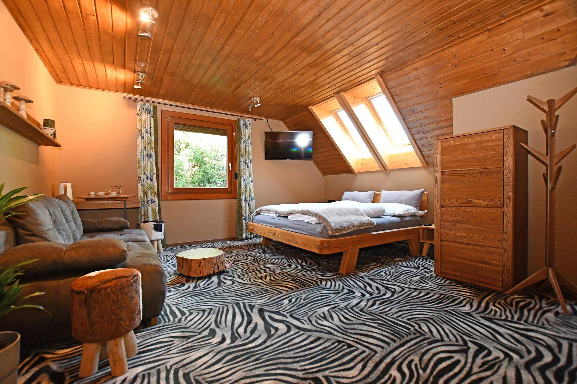 Gemütliches Schlafzimmer mit Holzbett, Sofa, Dachschrägen und auffälligem Teppichmuster.