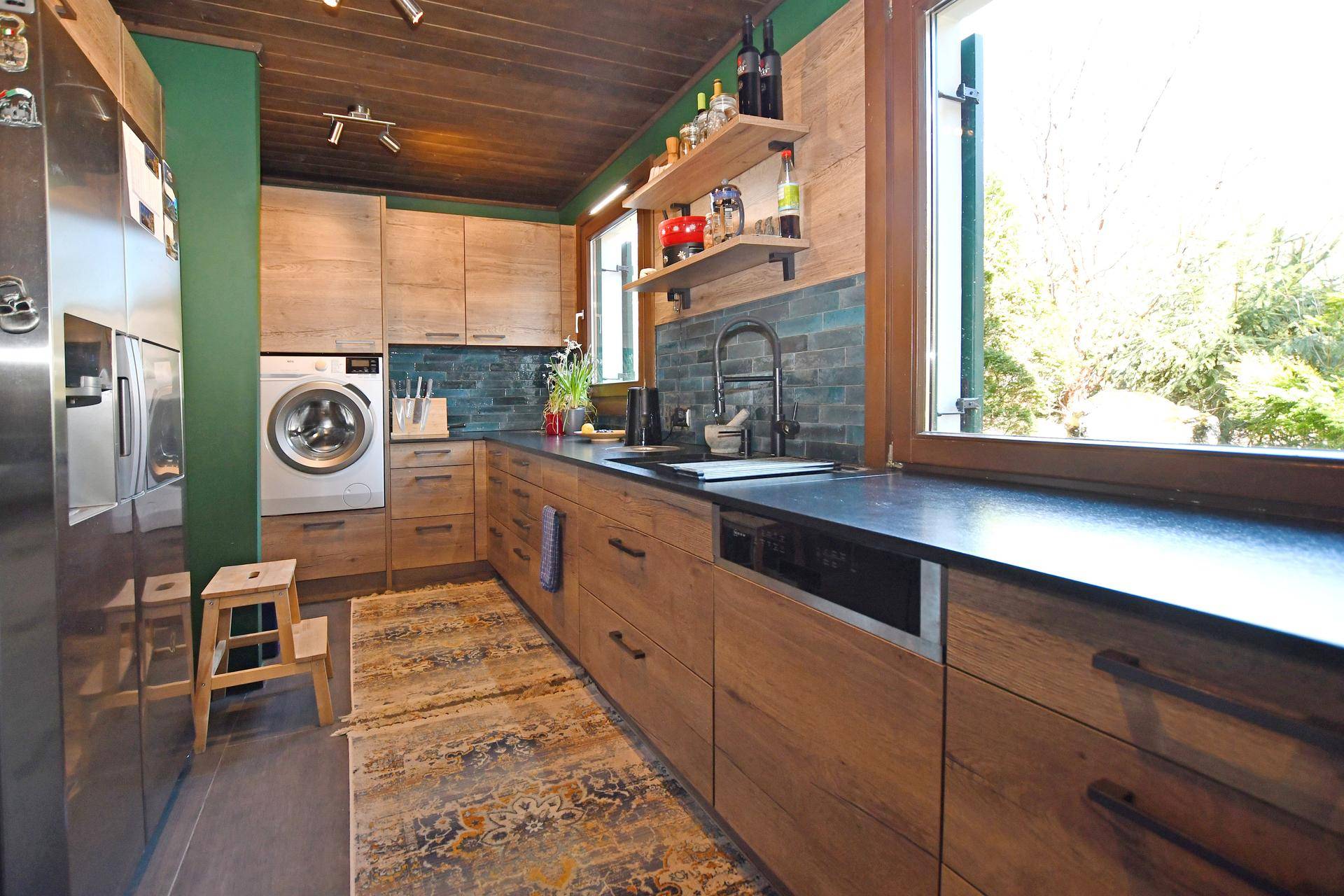 Moderne Holzküche mit integrierter Waschmaschine, dunkler Arbeitsplatte und grüner Wand.