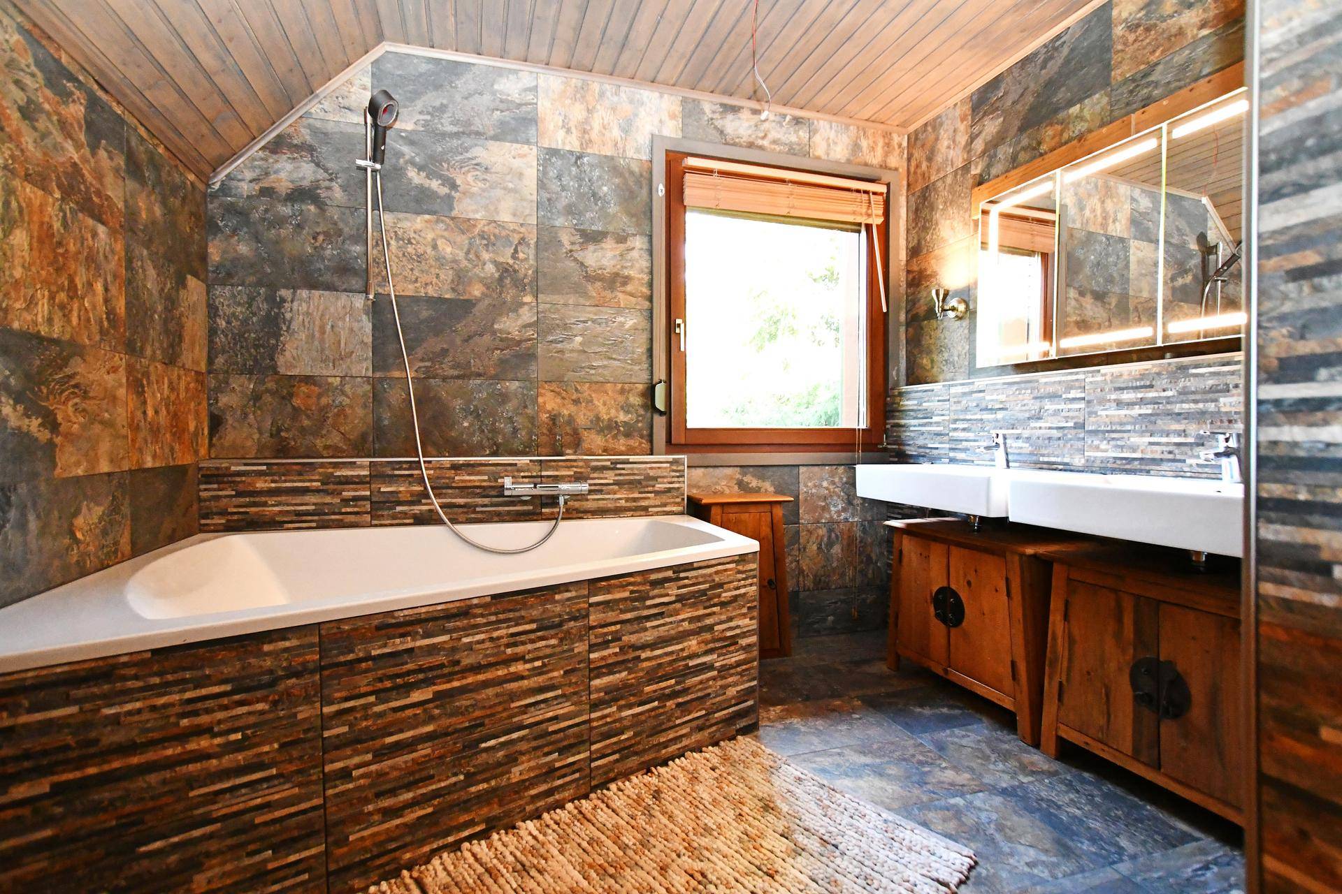 Modernes Badezimmer mit Eckbadewanne, Doppelwaschbecken und Natursteinfliesen an Wänden und Boden.