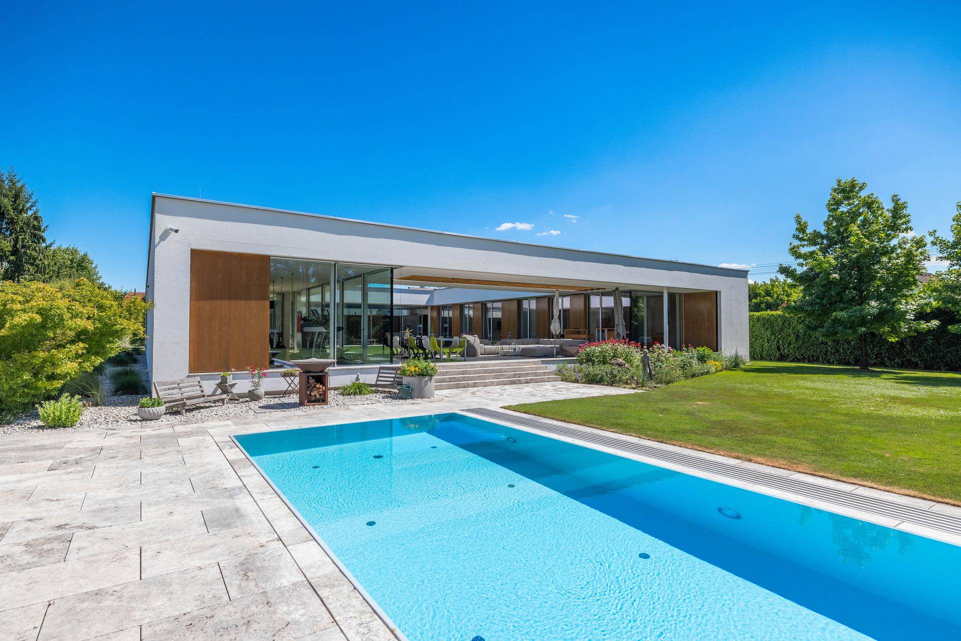 Elegantes modernes Haus mit großem Pool und weitläufigem Garten unter blauem Himmel.