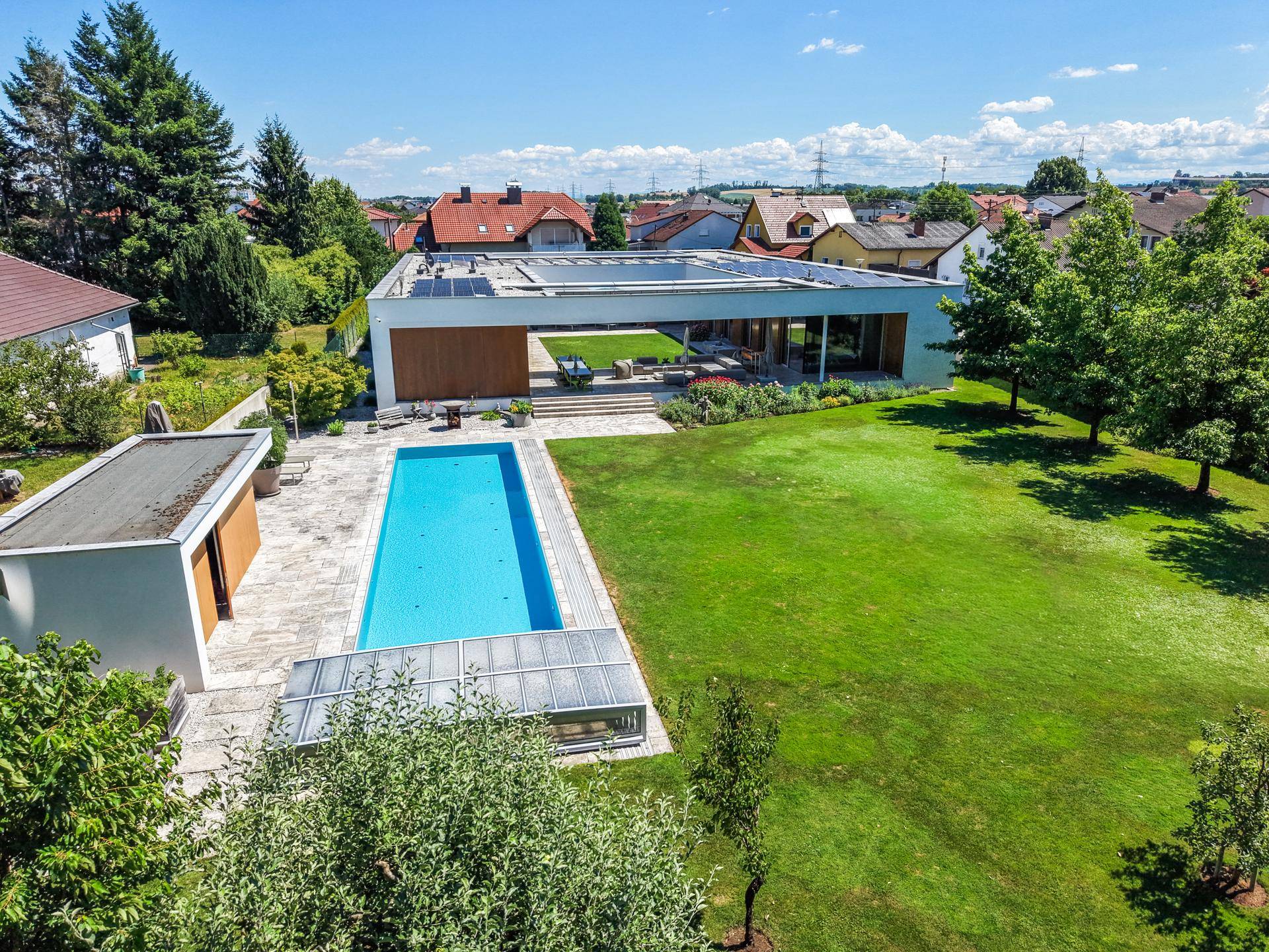 Luftaufnahme des modernen Anwesens mit großem Pool, weitläufigem Garten und umliegender Wohnbebauung.