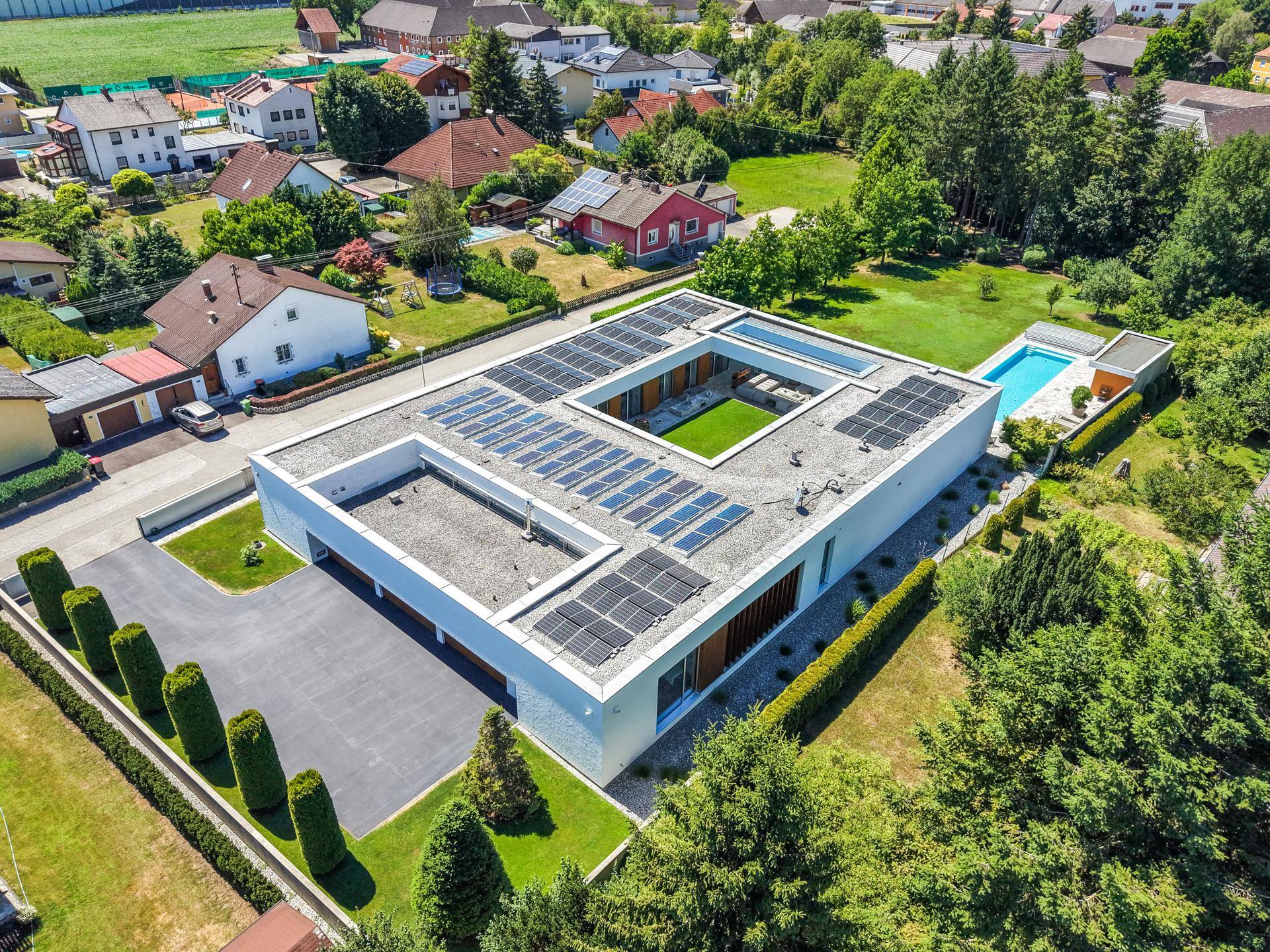 Gesamtansicht des modernen Hauses von oben mit Flachdach, Solaranlage und großem Grundstück.