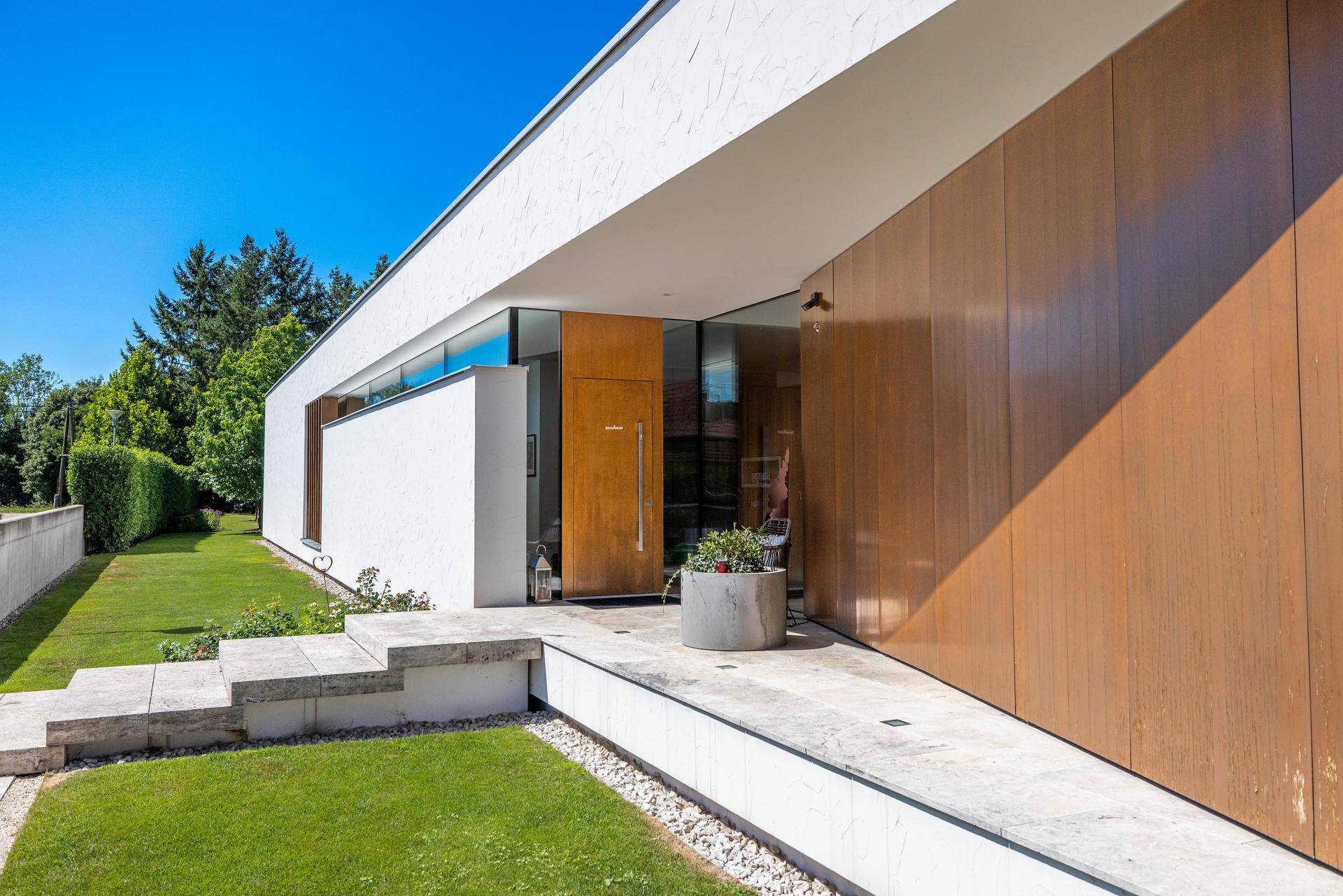Moderner Eingangsbereich des Hauses mit Rampe, Stufen und Holzelementen an der Fassade.