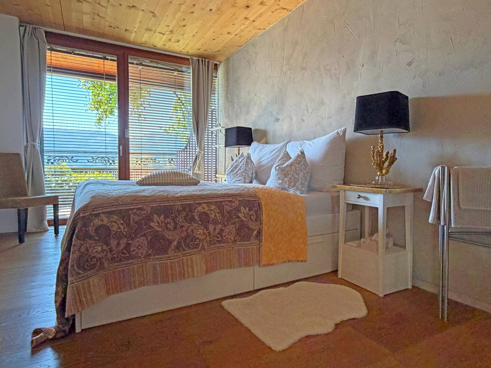 Gemütliches Schlafzimmer mit Holzboden, großen Fenstern und Blick ins Grüne.