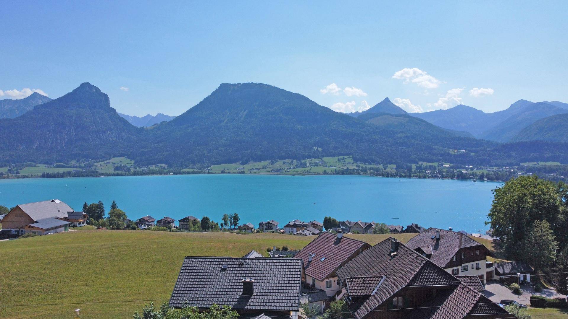 Weitläufiger Panoramablick auf den glitzernden See und die majestätischen Berge unter blauem Himmel.