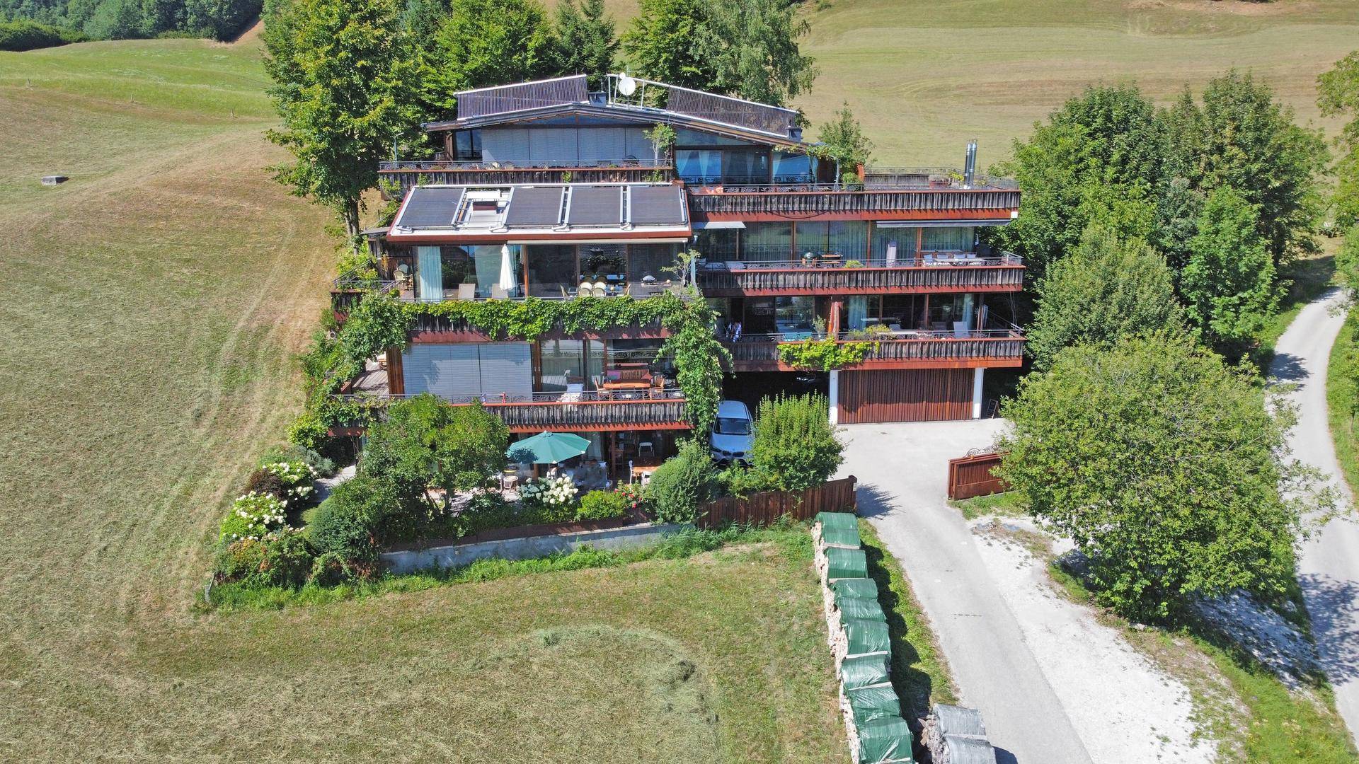 Luftaufnahme eines modernen Gebäudes mit mehreren Terrassen, umgeben von grünen Wiesen und Bäumen.