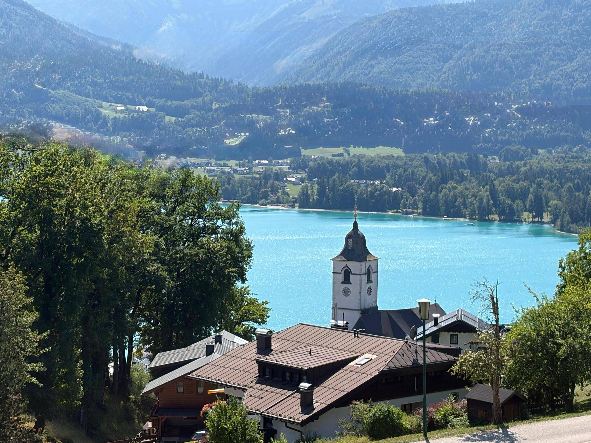 Malerischer Blick auf den türkisblauen See, umgeben von grünen Bergen und einem charmanten Kirchturm.