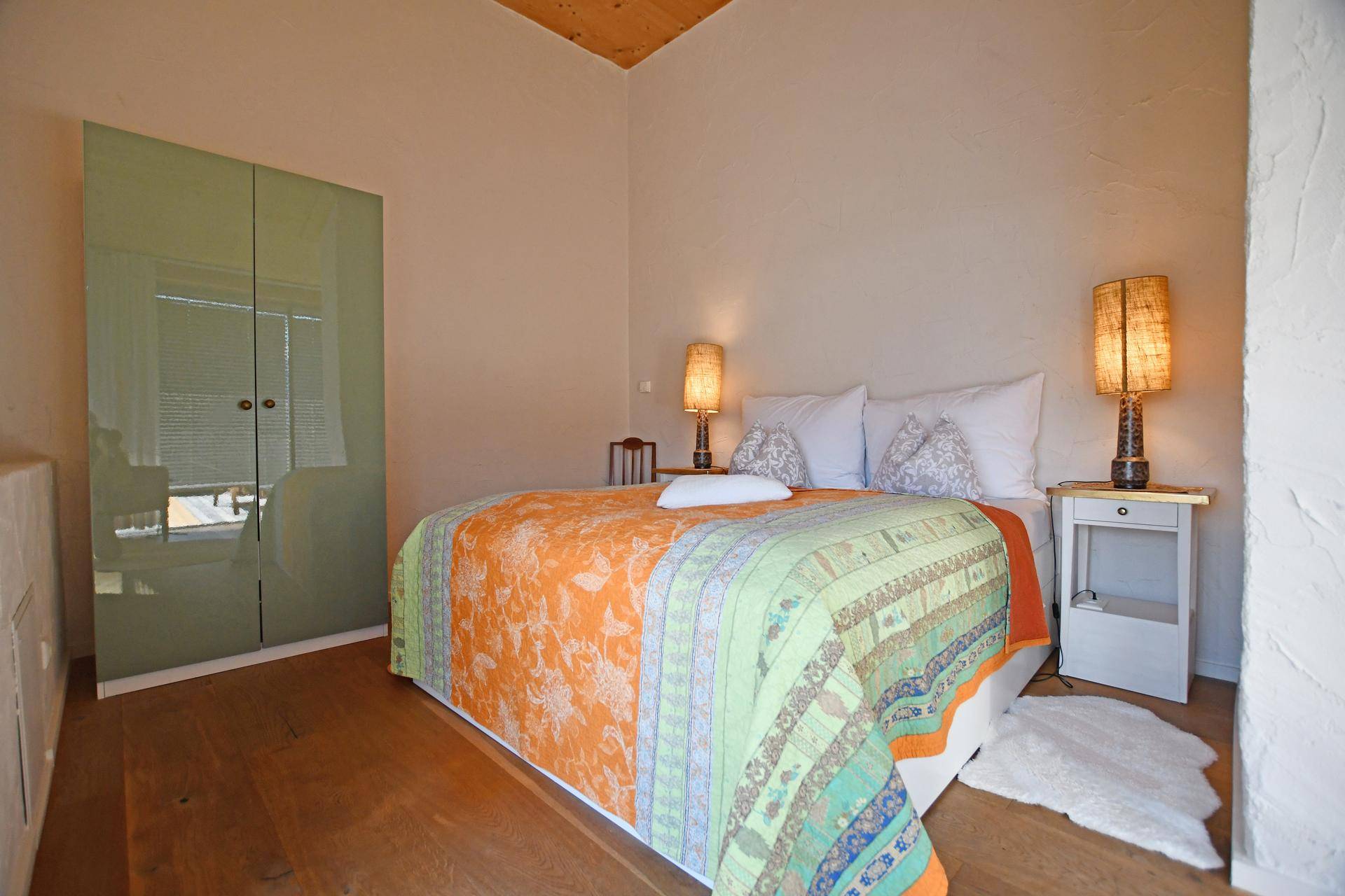 Helles Schlafzimmer mit farbenfroher Bettdecke, Holzboden und modernem Kleiderschrank.