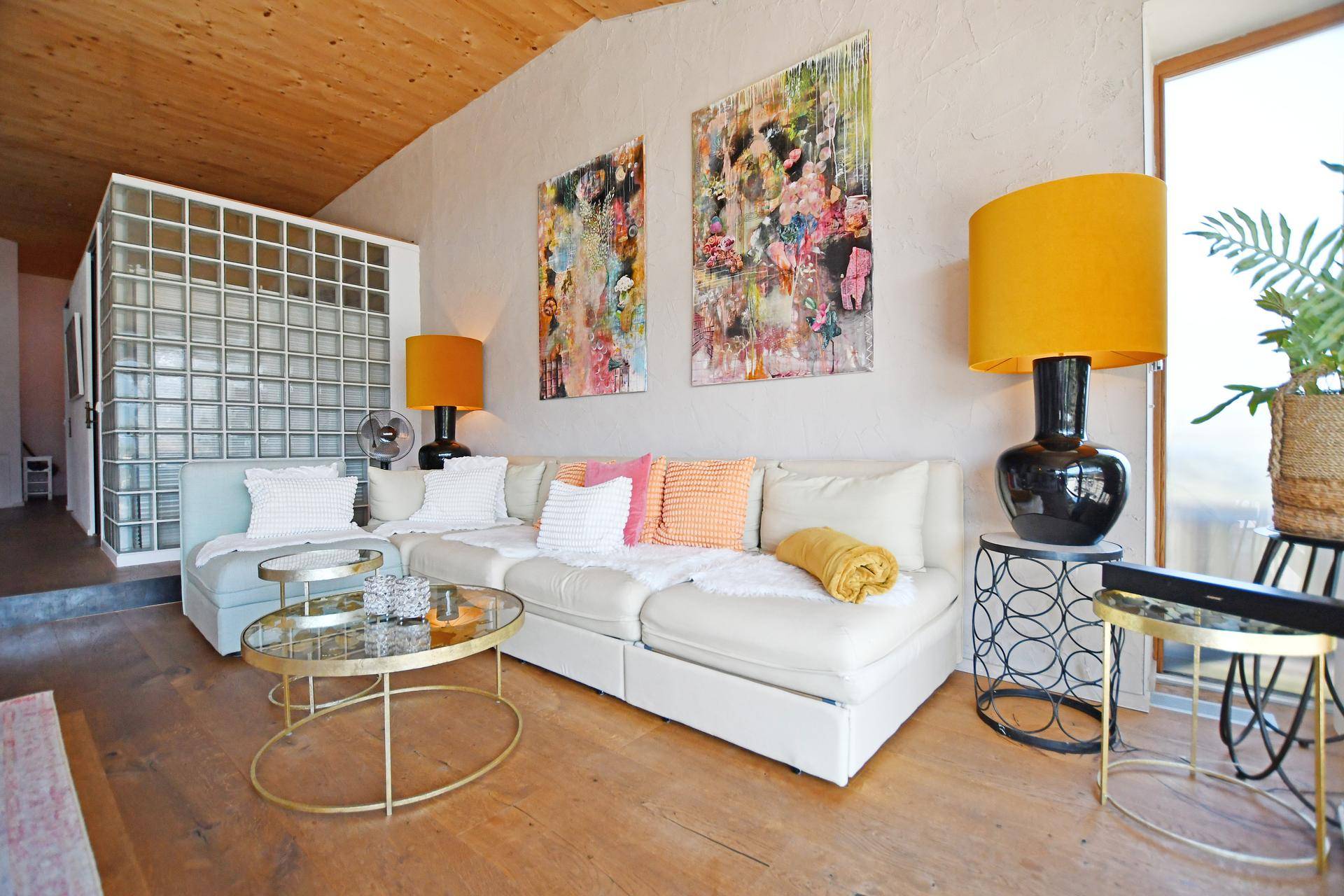 Helles Wohnzimmer mit bequemer Couch, farbenfroher Dekoration und Holzbalkendecke.