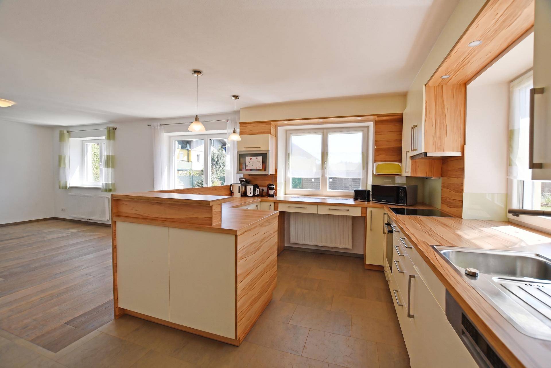 Moderne Küche mit Holztheke, integrierten Geräten und offenem Übergang zum Wohnbereich.