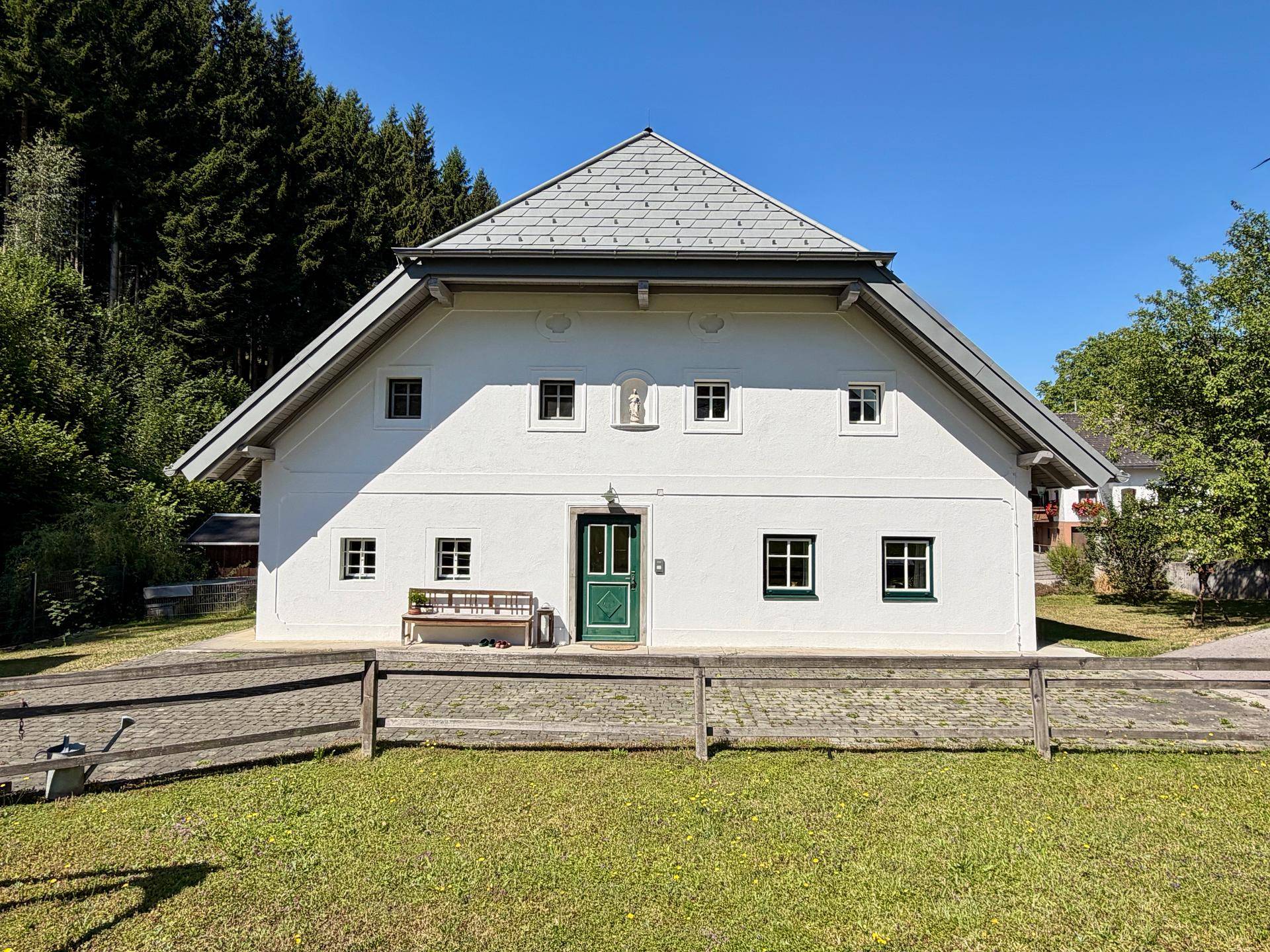 Frontansicht eines gepflegten weißen Landhauses mit grüner Eingangstür und Fenstern.
