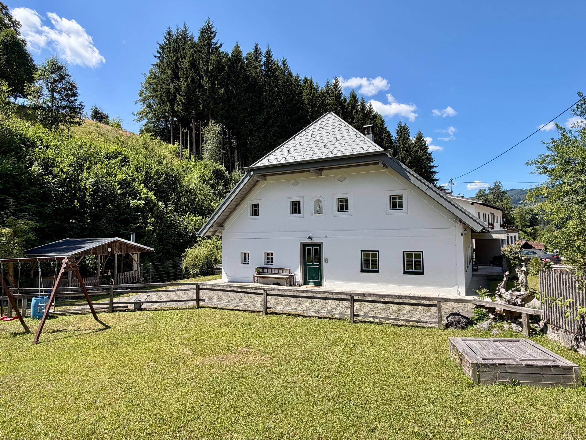 Landhaus mit großem Garten, Schaukel und Sandkasten, umgeben von Natur.