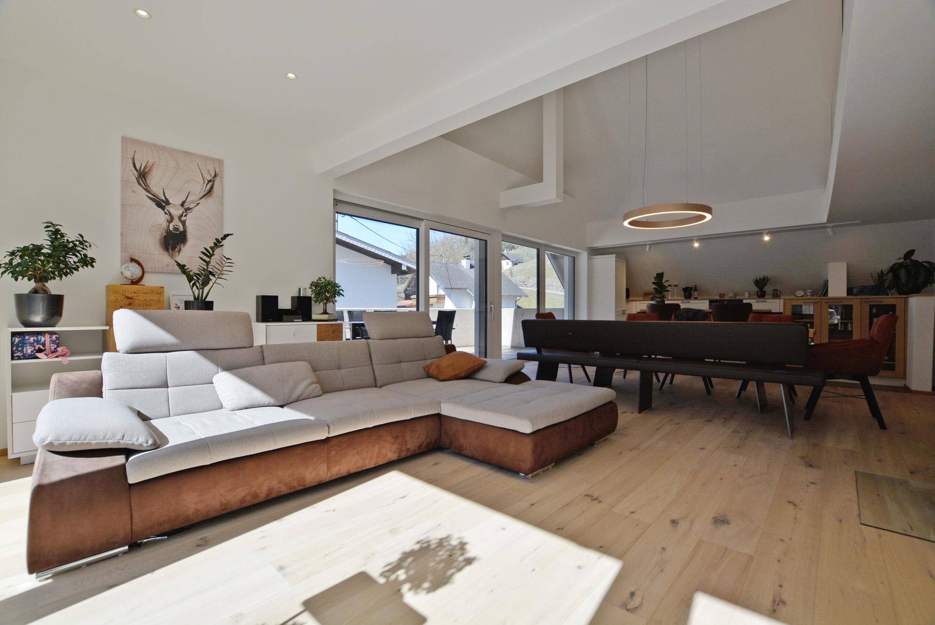 Helles, offenes Wohnzimmer mit großem Ecksofa, Holzboden und Zugang zur Terrasse.