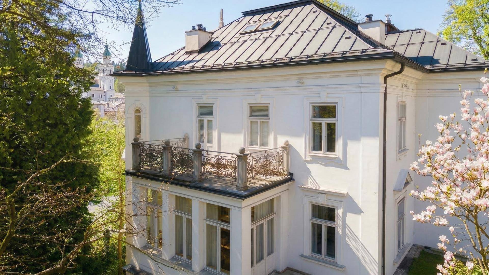 Detailansicht der eleganten weißen Fassade einer historischen Villa mit schmiedeeisernem Balkon und Mansarddach.