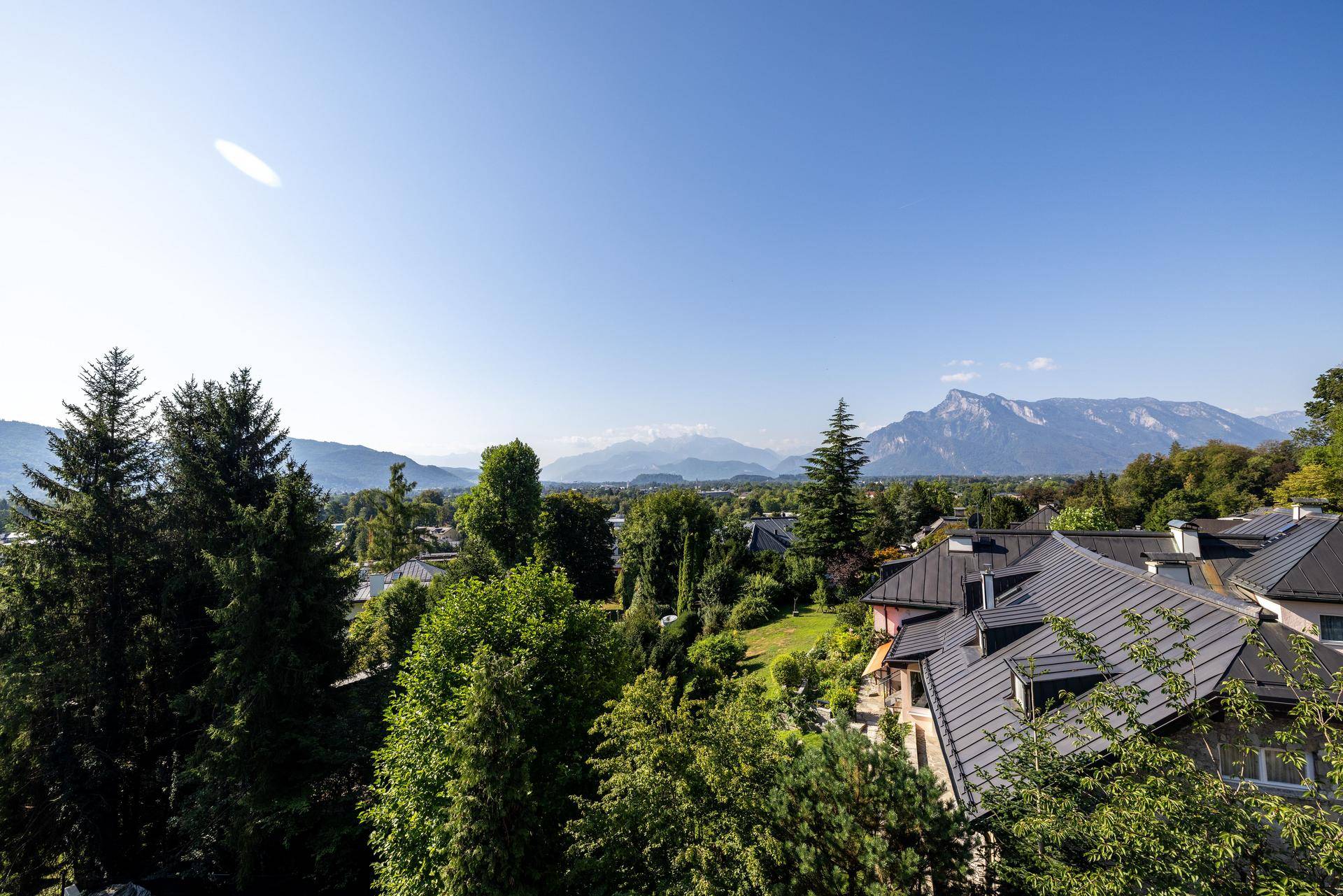 Panoramablick über eine grüne Landschaft mit Häusern und majestätischen Bergen im Hintergrund.