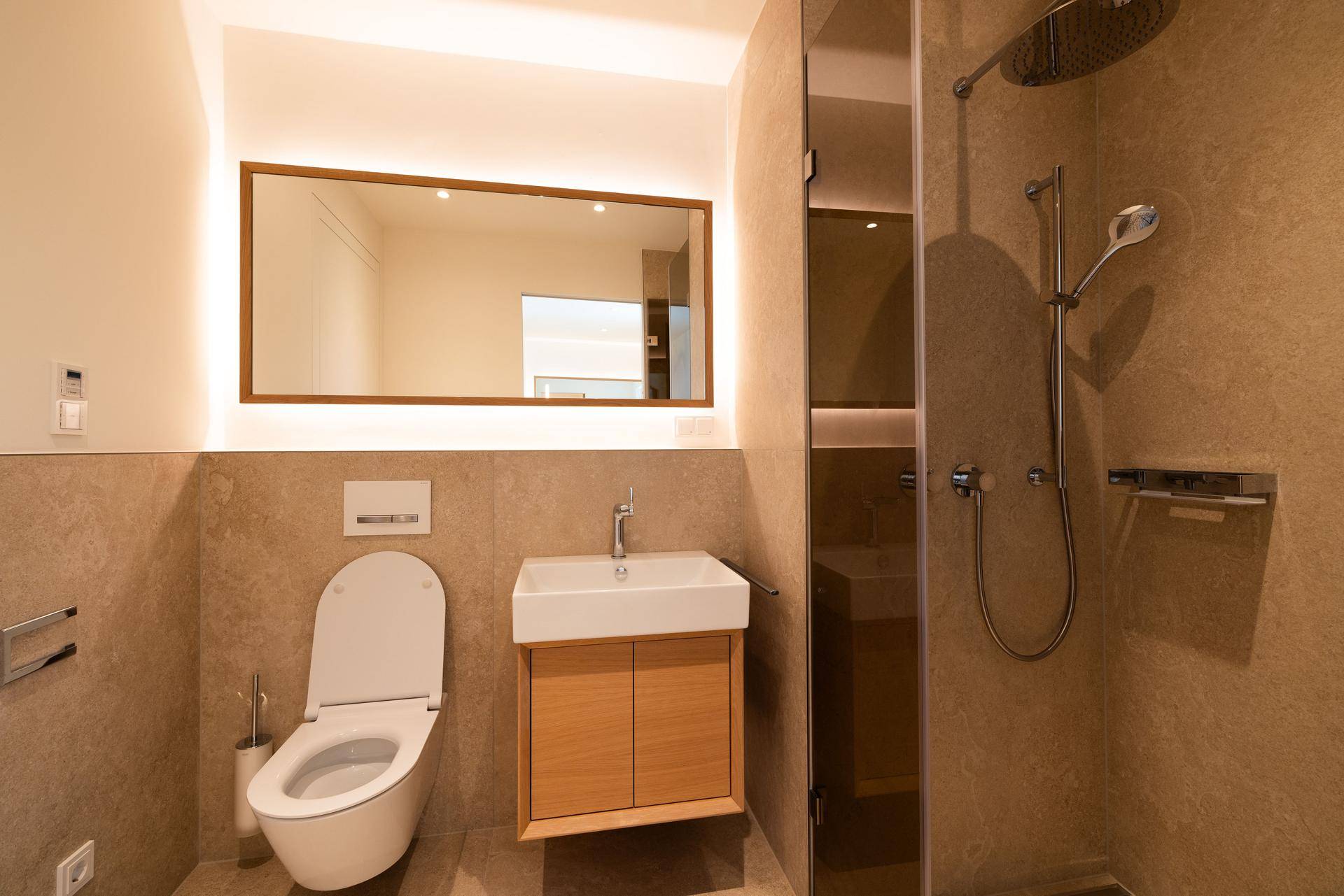 Modernes Badezimmer mit begehbarer Dusche, Wand-WC und einem elegant beleuchteten Spiegel.