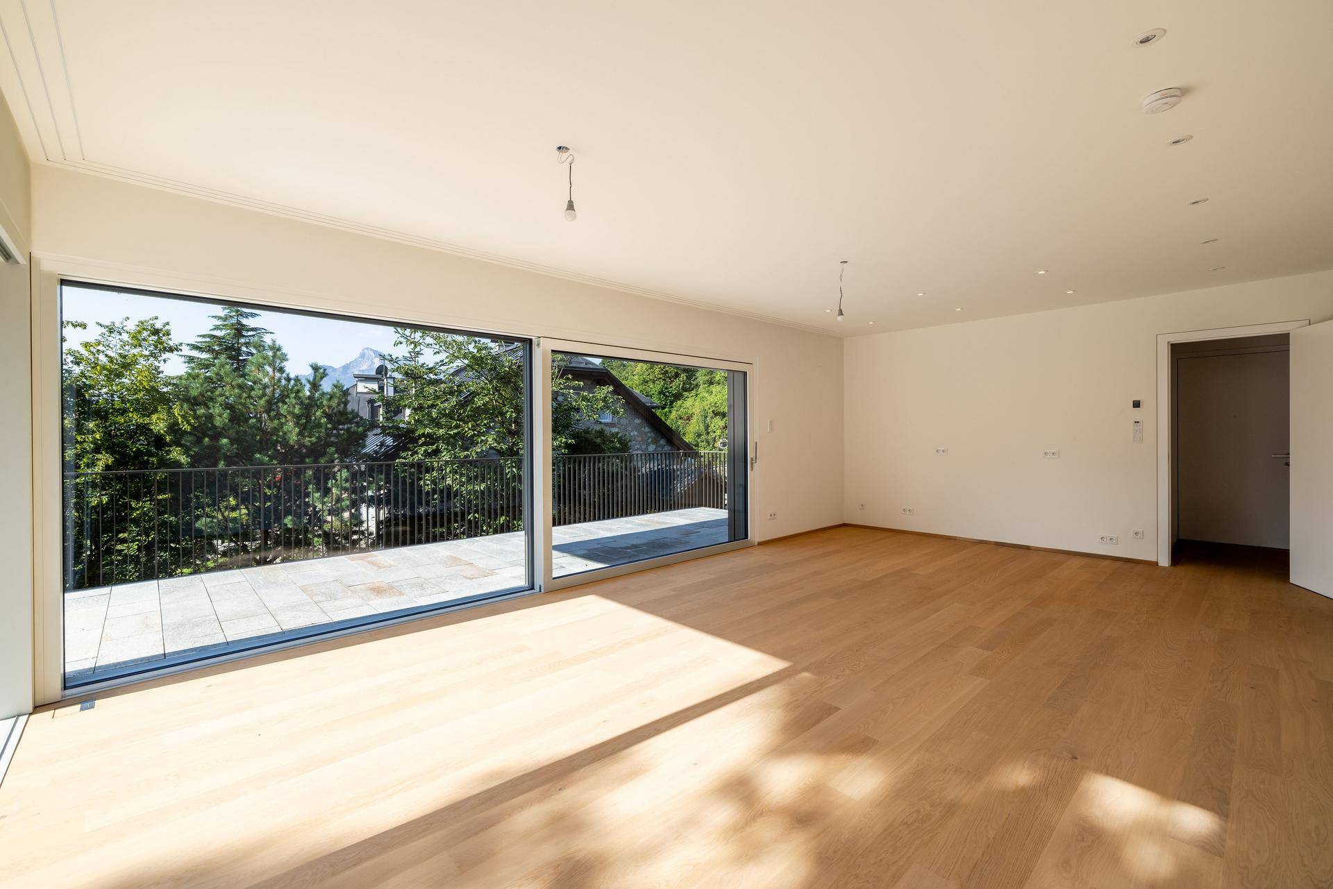 Lichtdurchfluteter Wohnbereich mit Holzboden und weitem Ausblick durch expansive Fensterfronten.