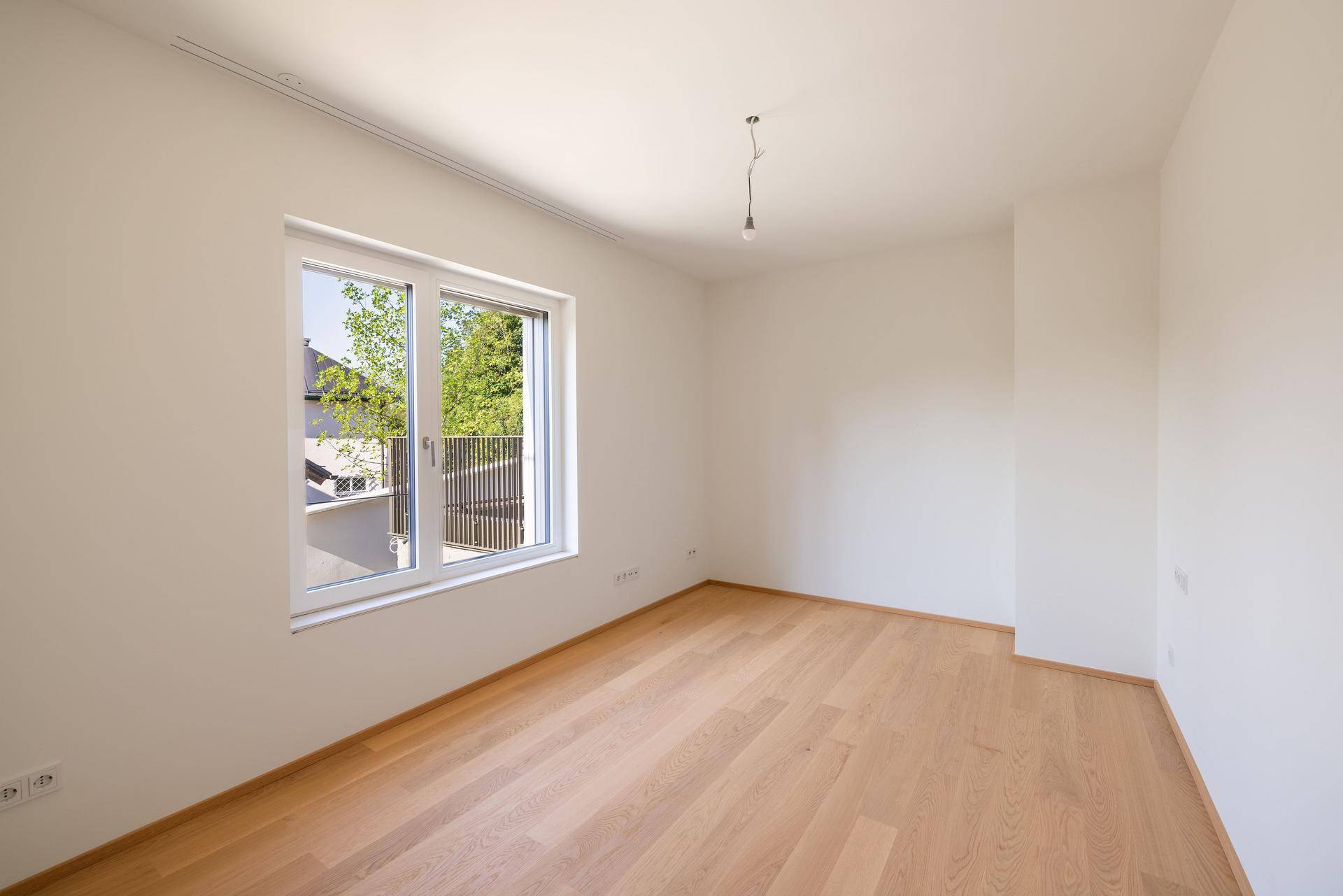 Ruhiges Schlafzimmer mit Holzboden und großem Fenster, das viel natürliches Licht hereinlässt.
